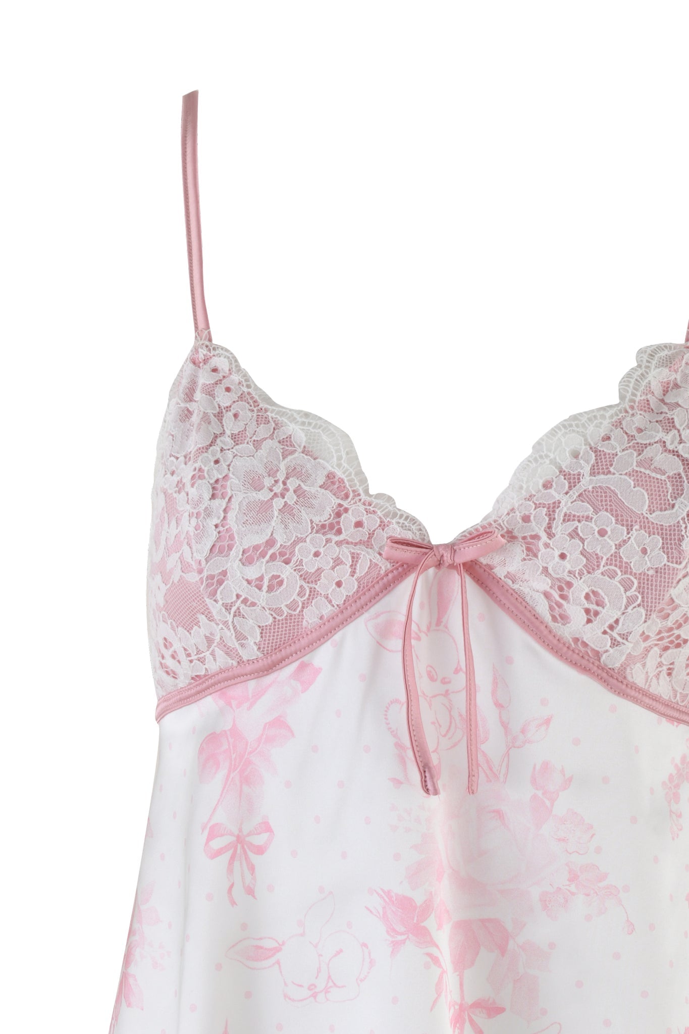 A detailed view of the Bridget Cami 2 Piece Set by I.AM.GIA reveals a delicate pink and white lace camisole with floral patterns, echoing the charm of vintage slip dresses. It boasts thin pink straps and a small central bow, complemented by intricate lace detailing at the top. The fabric showcases subtle floral prints.