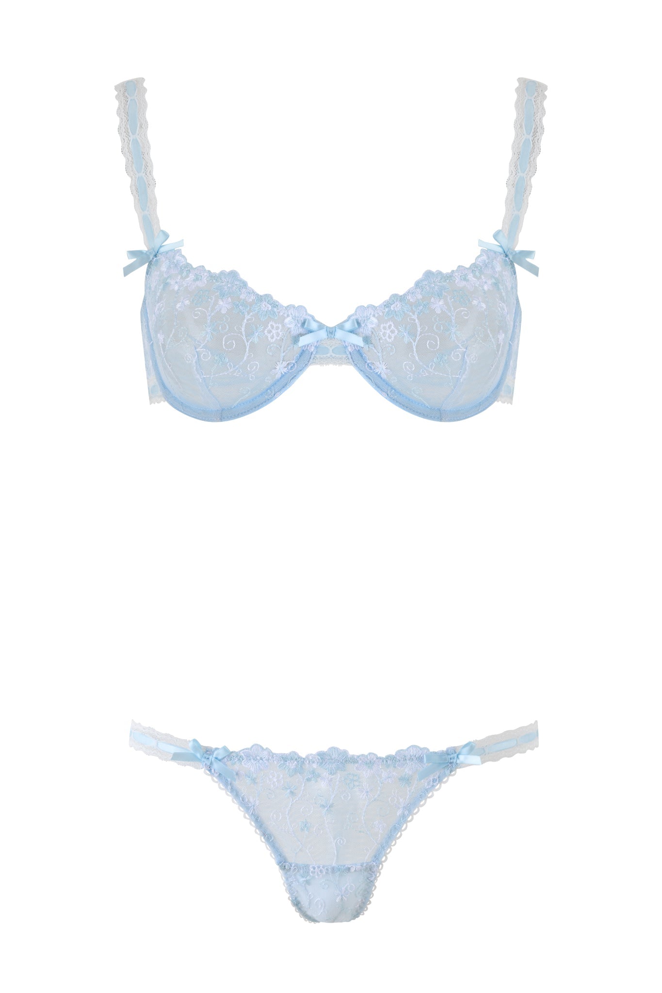 The ROMY 2 PIECE SET - BLUE by I.AM.GIA is a light blue lace lingerie set, including a bra and panties, adorned with floral lace and small ribbon bows on the straps. The panties feature an embroidered daisy lace pattern and a central bow.