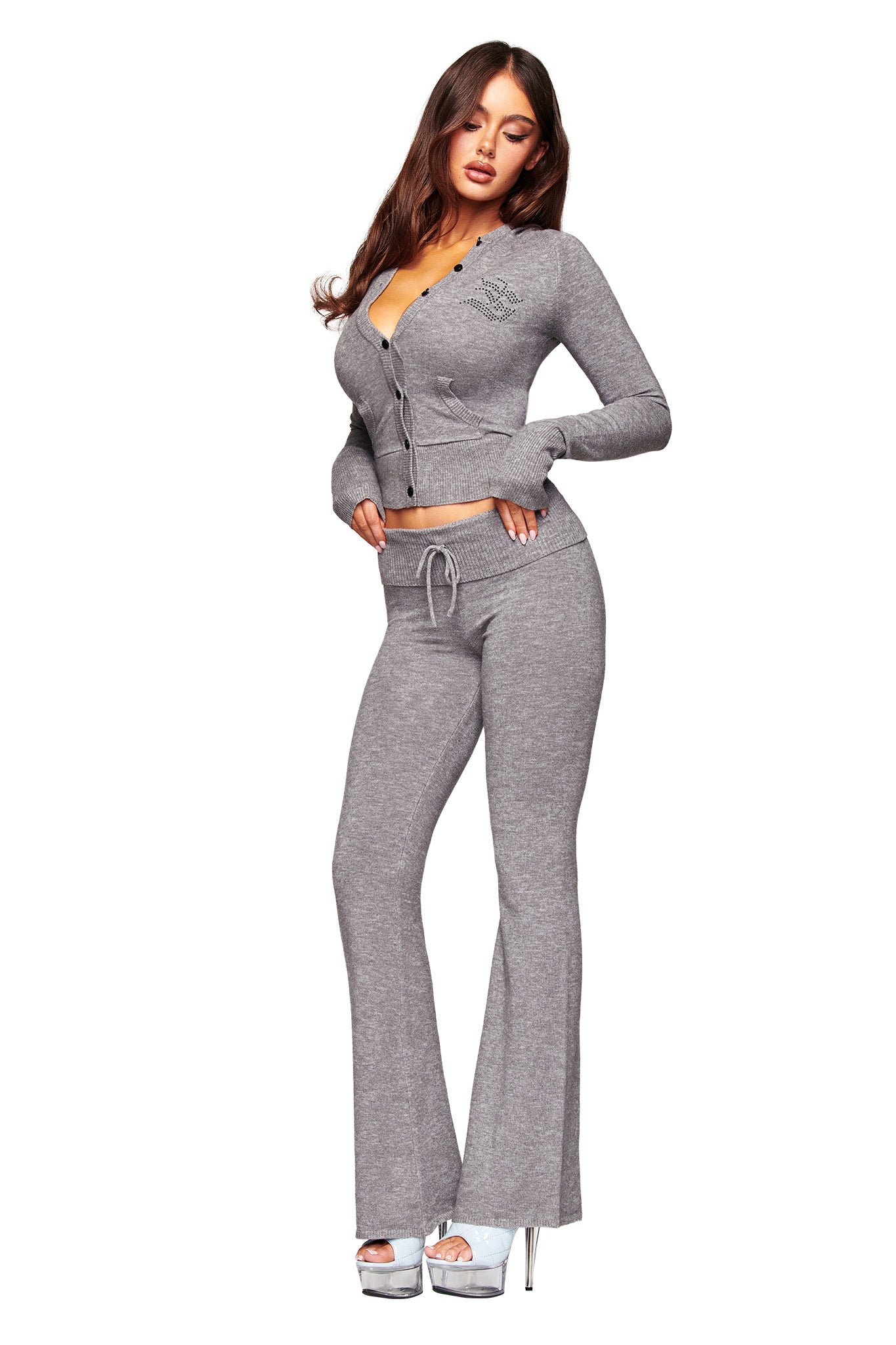 A woman poses in the I.AM.GIA JESSA PANT - GREY, featuring flared legs and a drawstring waist, styled with a matching light gray knit cardigan and silver high heels against a white background.