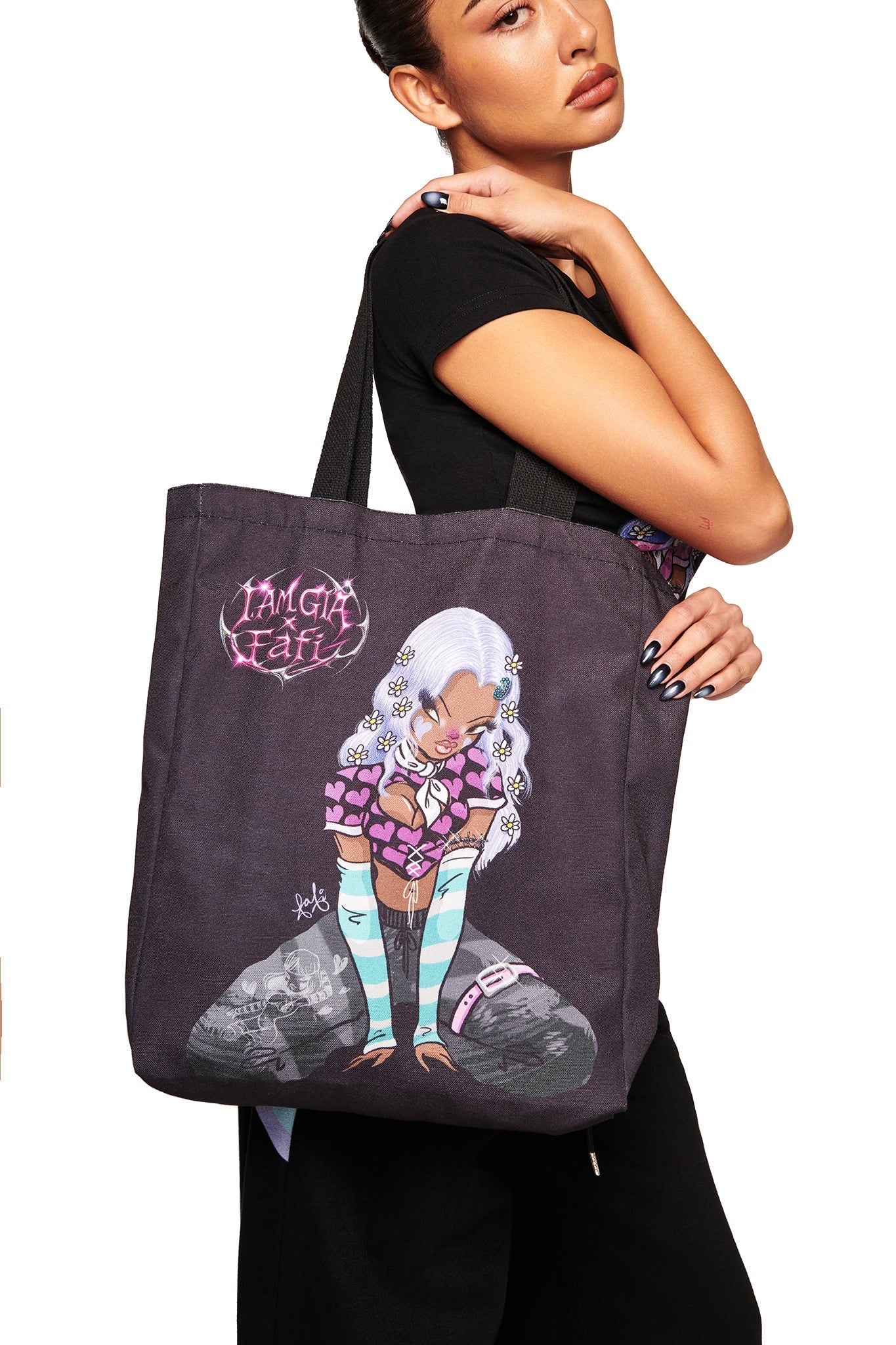 A woman holds the FAFI TOTE BAG - BLACK by I.AM.GIA, featuring colorful artwork of a stylized girl with long white hair in striped socks, surrounded by pink hearts and exclusive “I'M GIA FEATI” text above the design.