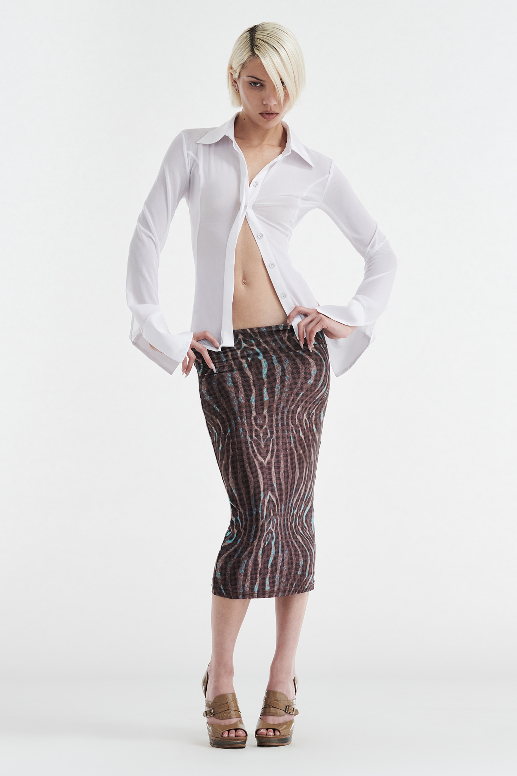 A person with short blond hair models the CDP GISELLE STRETCH MIDI TUBE SKIRT in Warped Check, paired with a white shirt and tan platform sandals, posed against a plain white background.