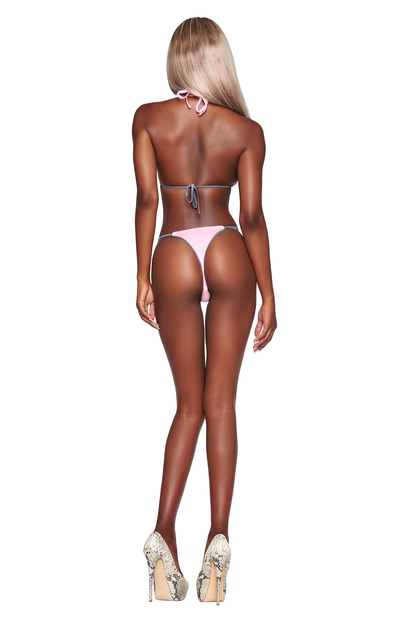 A person with long blonde hair stands facing away, wearing the I.AM.GIA CAMERON BIKINI BOTTOM in baby pink and high heels with a snakeskin pattern, against a plain white background.