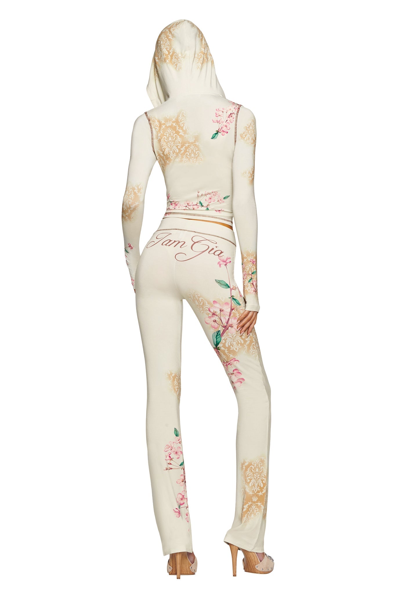 A person is seen from behind in high heels, wearing the I.AM.GIA BLARE HOODIE in blossom print with matching pants, featuring “I.AM.GIA” branding on the back.