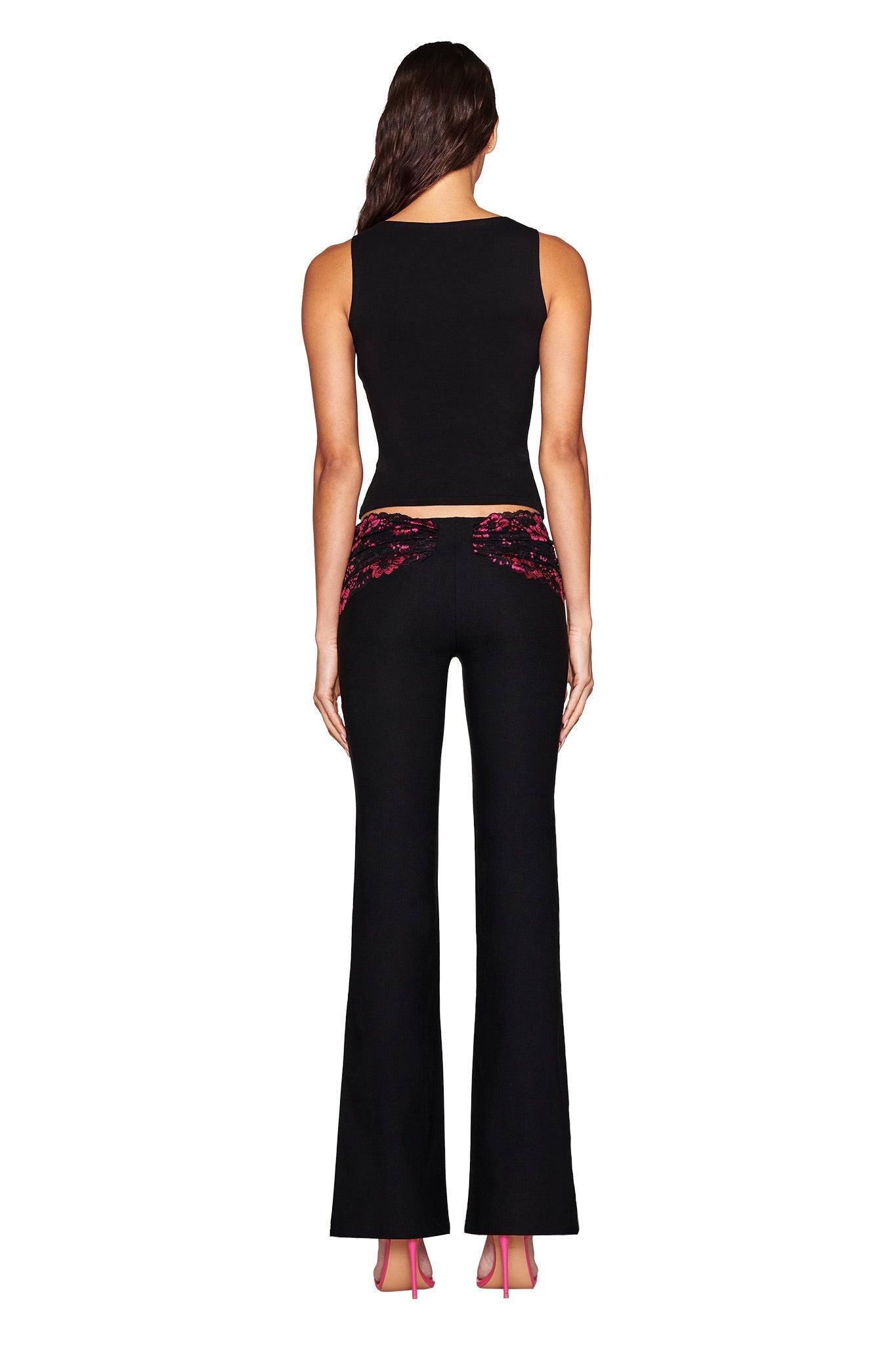 A person with long hair wears a black sleeveless top and I.AM.GIA's ANGELINA PANT in black with lace pink sequined pocket details, paired with pink high-heeled shoes against a white background.