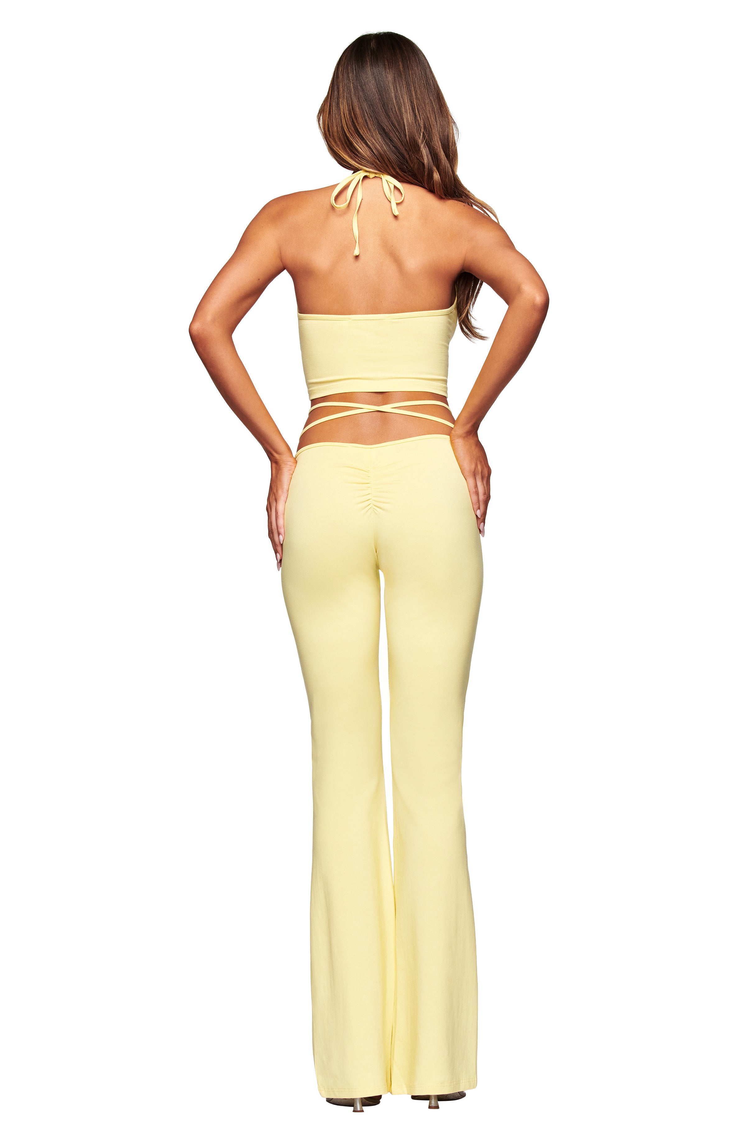 A woman with long brown hair is seen from the back wearing the I.AM.GIA HALO TOP - BUTTER YELLOW halter top with matching high-waisted flared pants, set against a white background.
