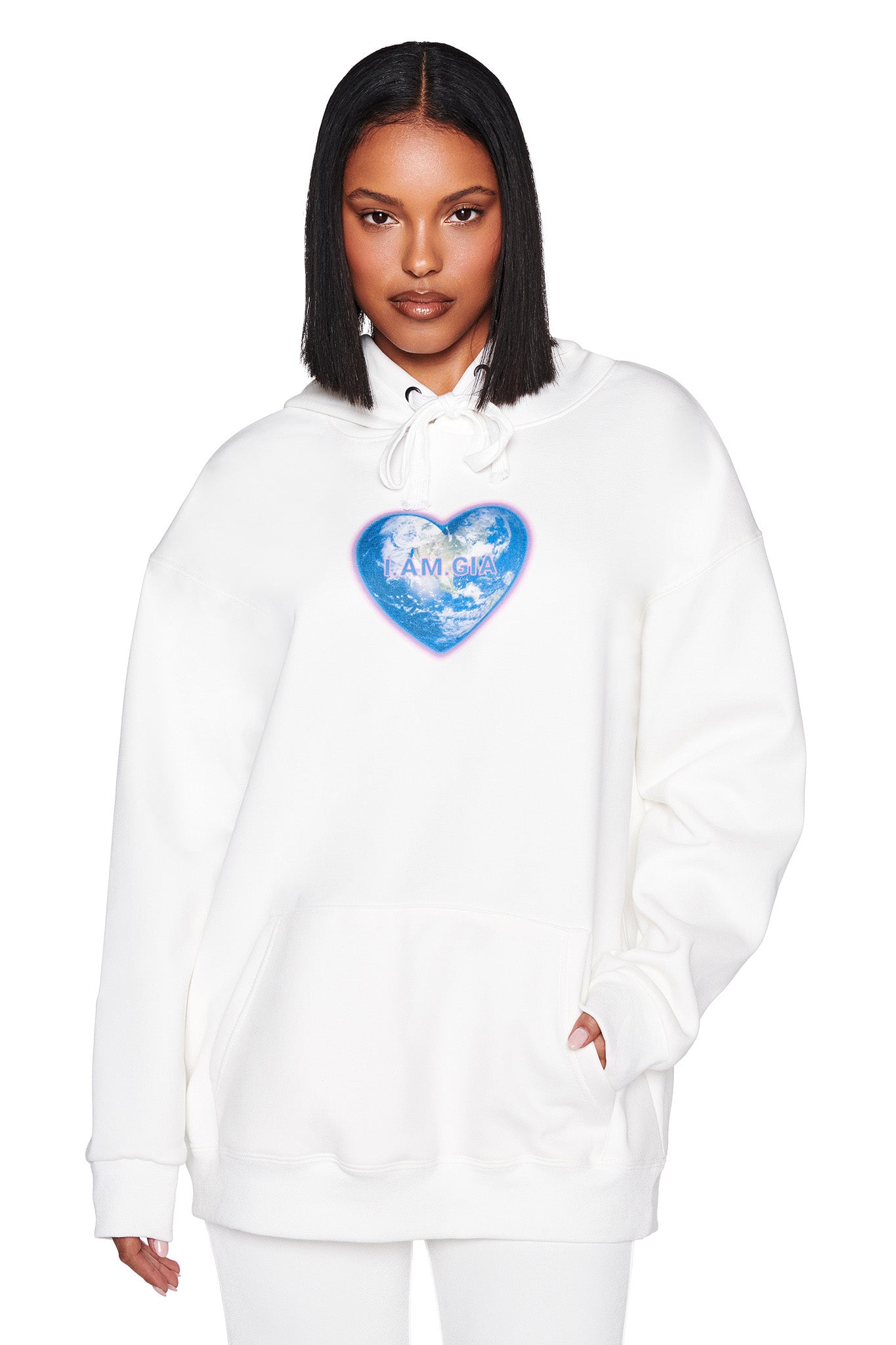A person with shoulder-length black hair is wearing the HARMONY HOODIE - WHITE by I.AM.GIA, featuring a blue heart and the words "I AM GAY," complete with a front pocket.