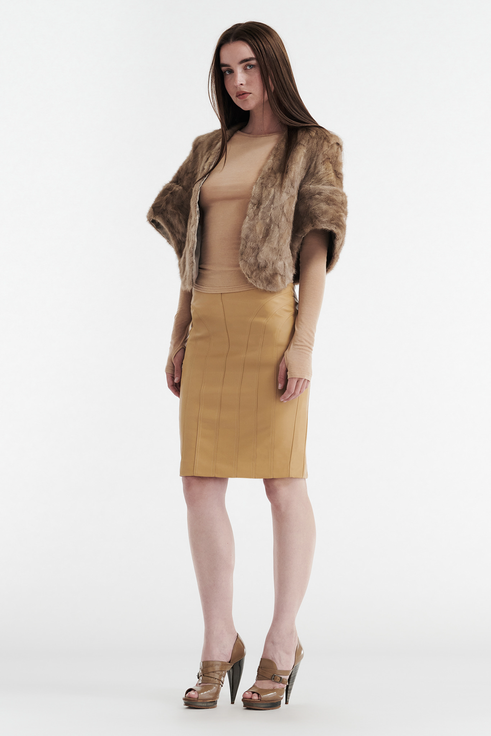 A woman stands against a white background wearing a tan long-sleeve top, the CDP INES FAUX LEATHER PENCIL SKIRT in tan, a brown faux fur shawl, and tan high-heeled shoes. She faces forward with a neutral expression.