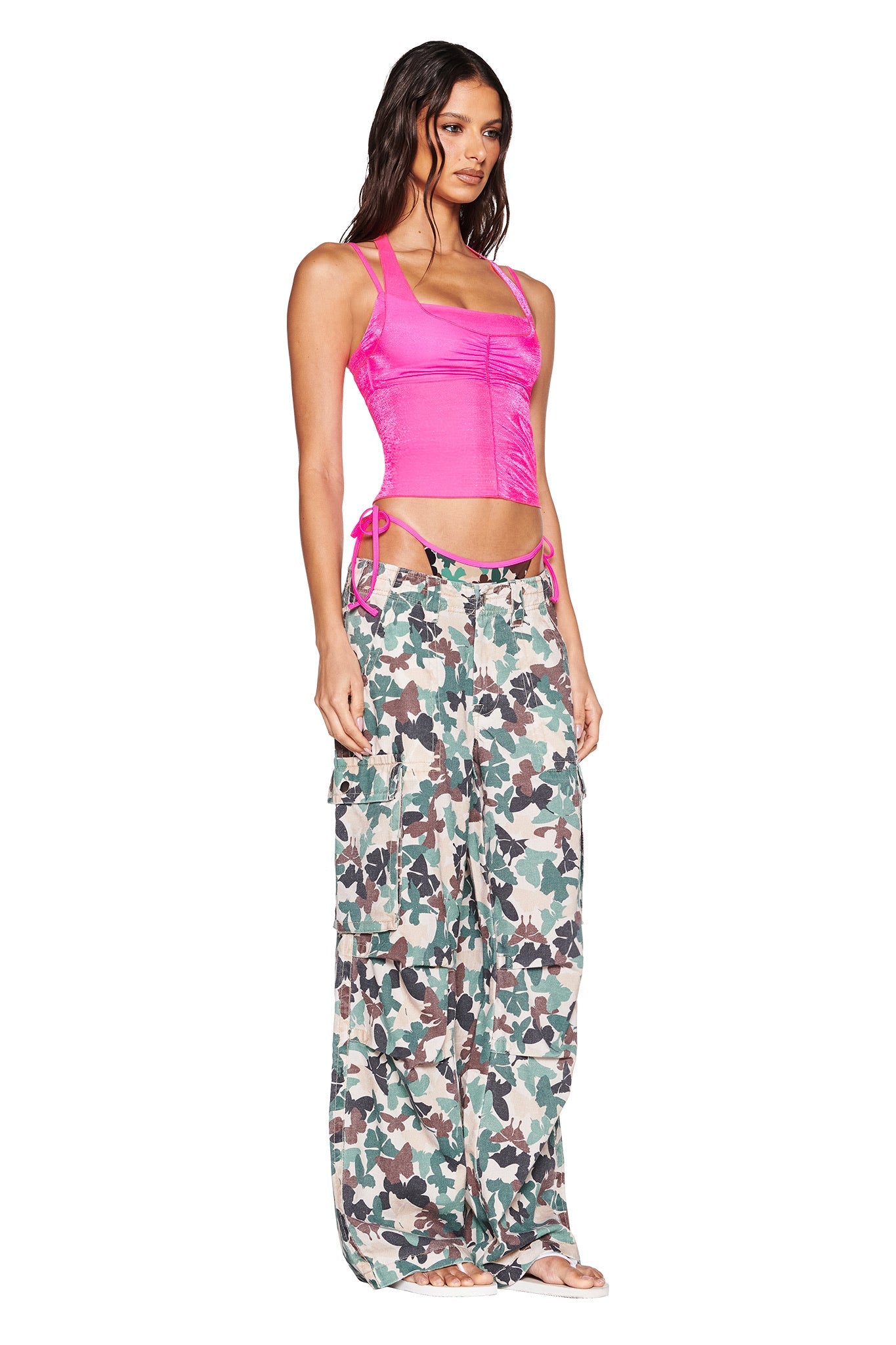 A person in an I.AM.GIA NERINA TOP - NEON PINK with side ties and green camouflage cargo pants stands against a plain white background.
