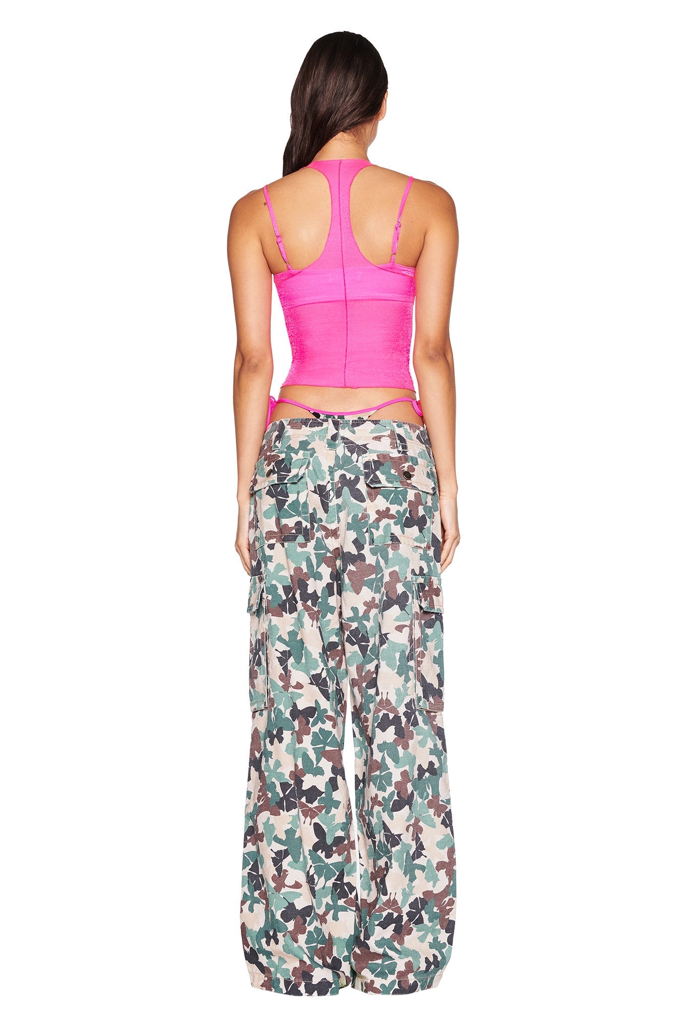 A person with long brown hair is shown from the back wearing the I.AM.GIA NERINA TOP - NEON PINK paired with baggy camouflage cargo pants against a plain white background.