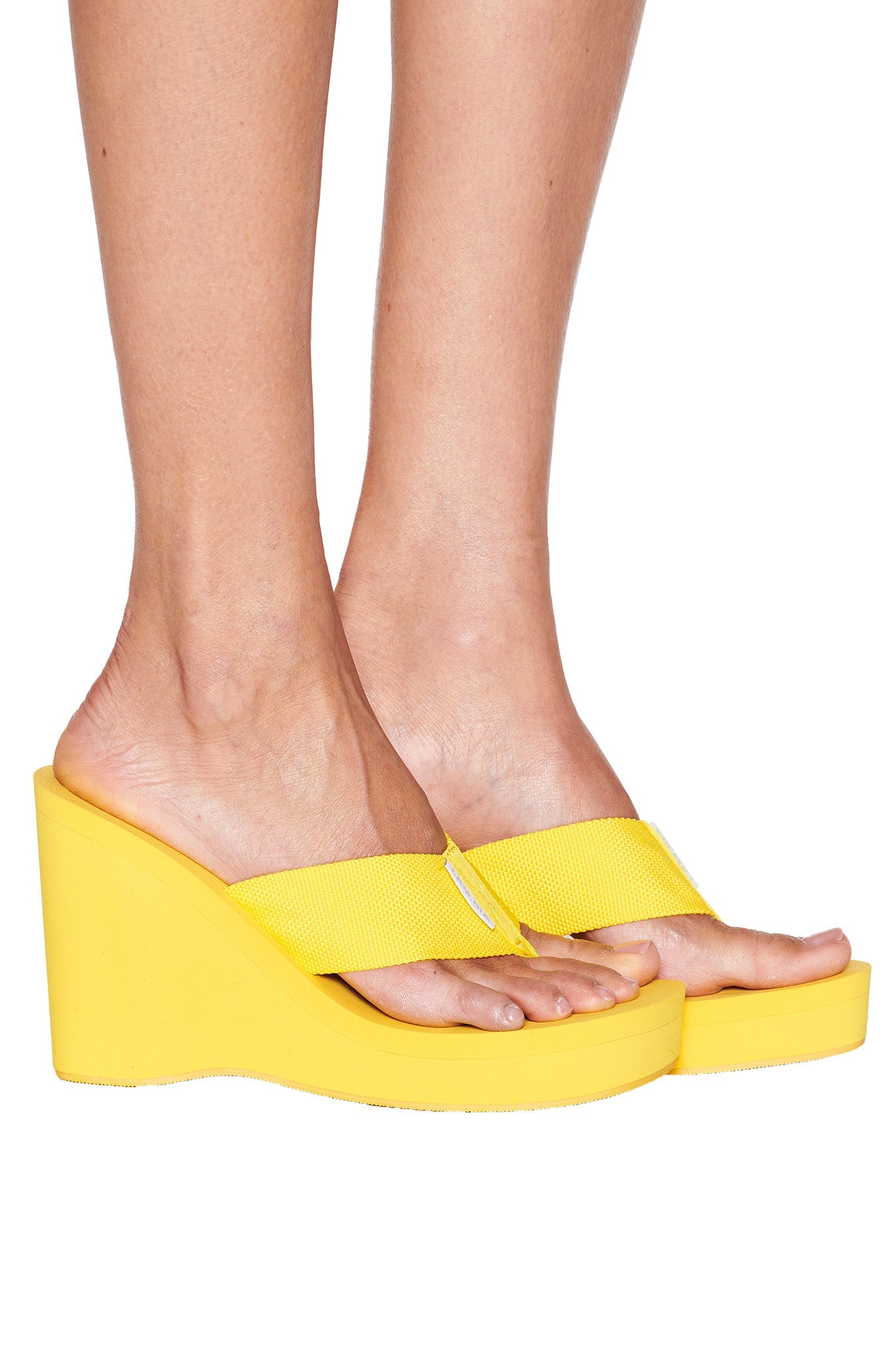 Someone models the I.AM.GIA SHELBY FLIP FLOP in bright yellow, featuring thick straps, with their feet and lower legs visible against a plain white background.