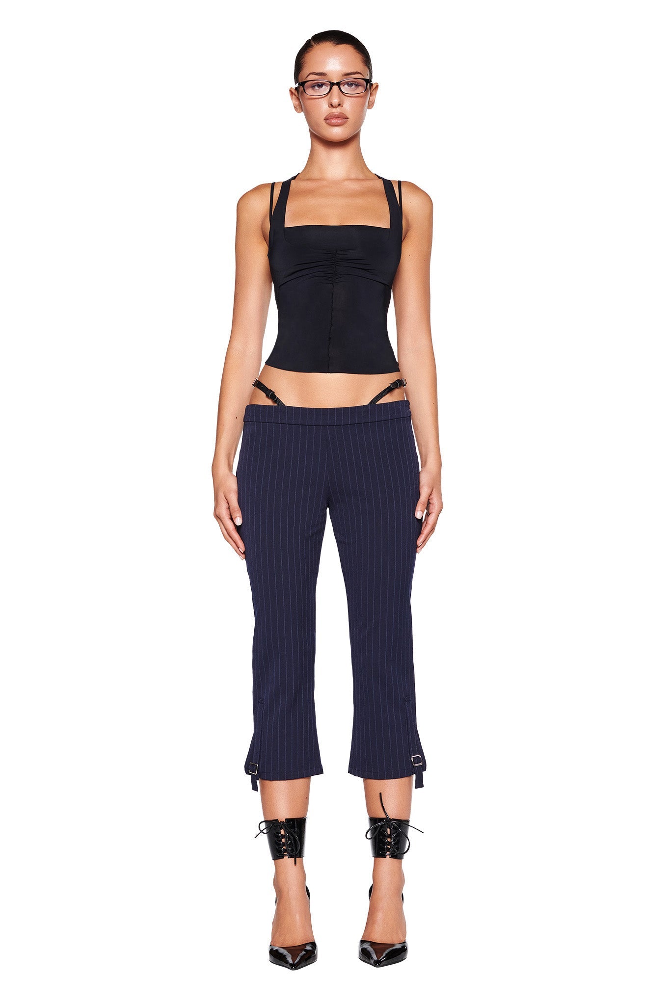Close-up of the lower part of the MARRION CAPRI - BLUE : PINSTRIPE by I.AM.GIA, showcasing fine vertical stripes. These navy capris feature a strap with a small silver buckle near the bottom hem of each leg, enhancing the adjustable side straps and straight leg silhouette.