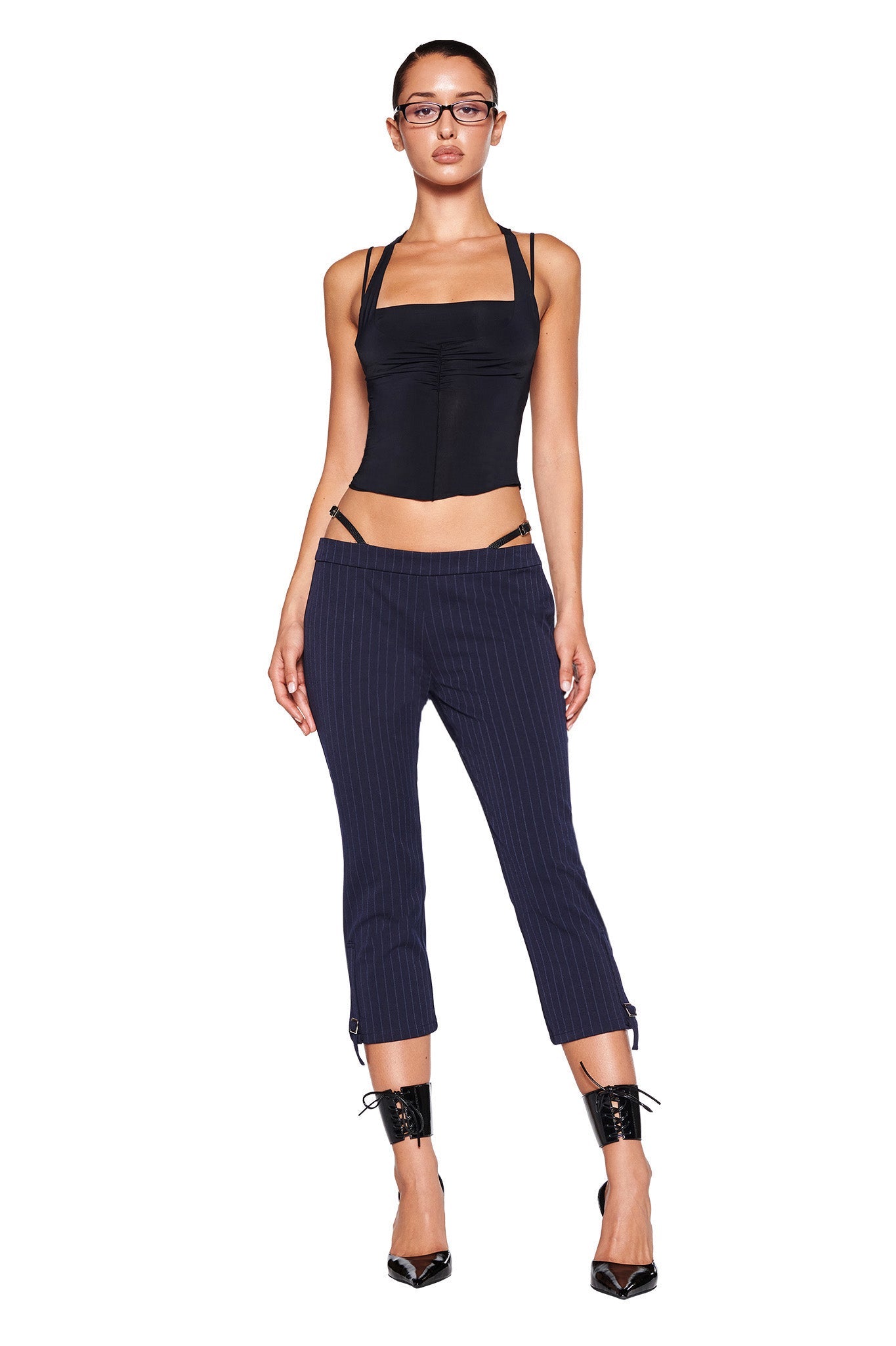 Close-up of the lower part of the MARRION CAPRI - BLUE : PINSTRIPE by I.AM.GIA, showcasing fine vertical stripes. These navy capris feature a strap with a small silver buckle near the bottom hem of each leg, enhancing the adjustable side straps and straight leg silhouette.