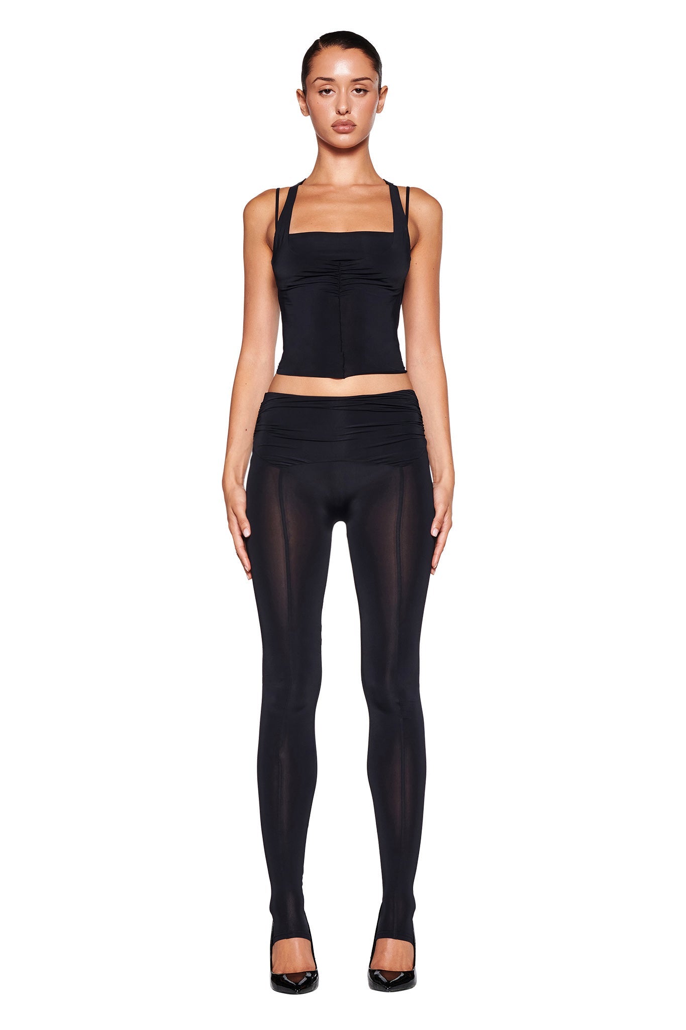 Image of the NERINA TIGHTS - BLACK by I.AM.GIA. These high-waisted leggings feature a bodycon fit with smooth, slightly sheer fabric on the lower legs. The wide waistband is ruched at the sides for added detail, providing a sleek and snug fit designed for both comfort and style.