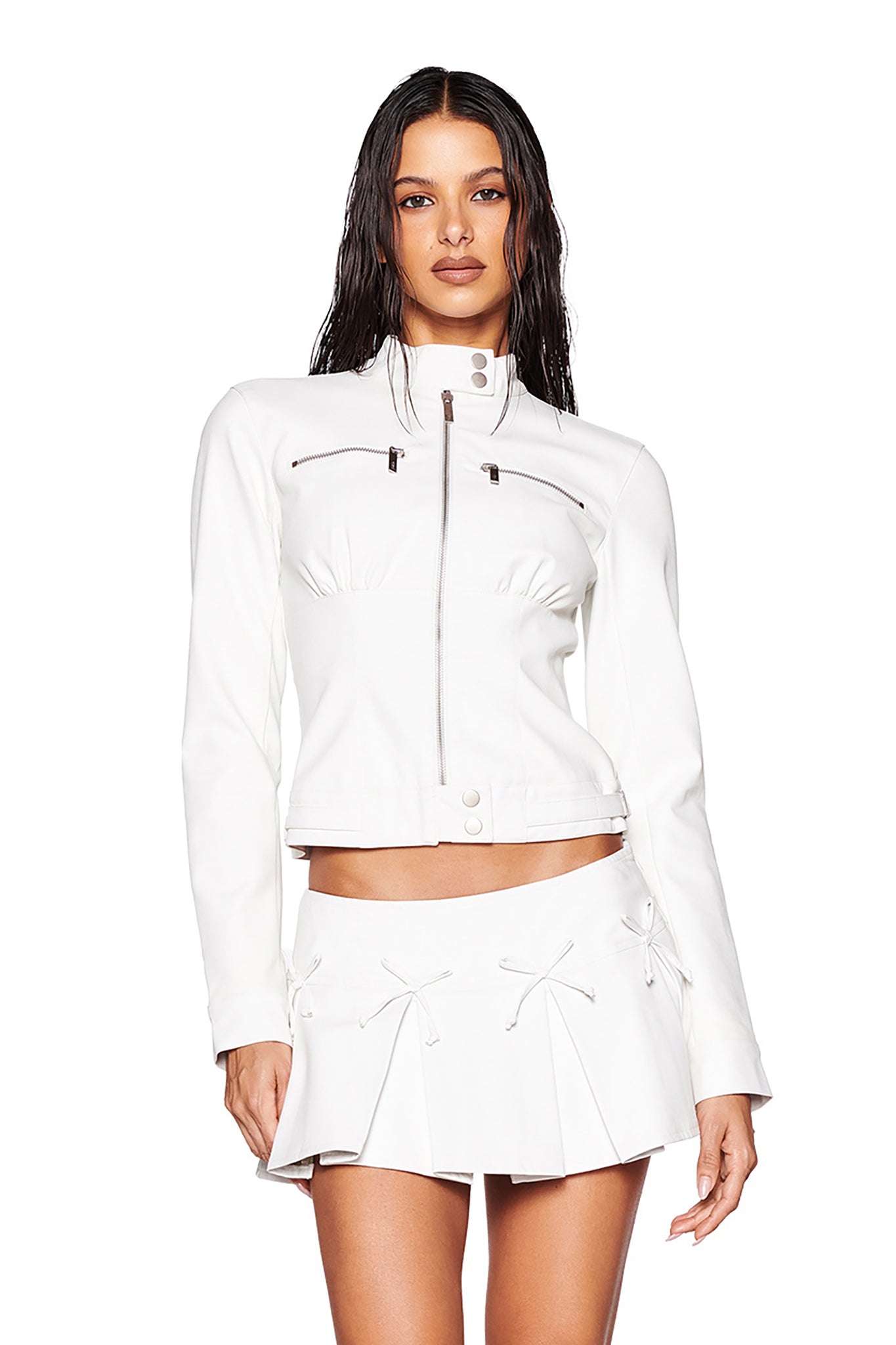 A person with wet, wavy hair is wearing the EVERETTE JACKET by I.AM.GIA in a chic moto style featuring zipper details, paired with a pleated mini skirt. The fitted silhouette stands out against the plain white background.
