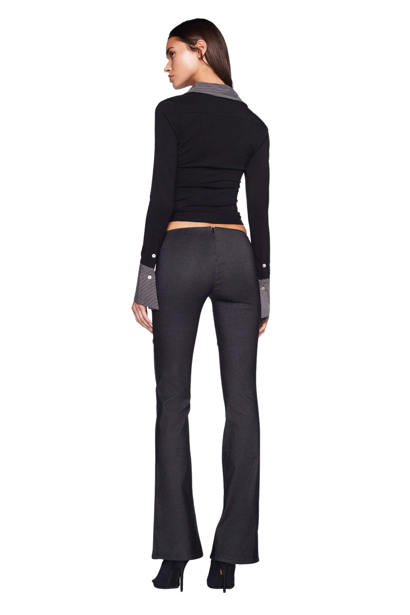 A person with long brown hair stands with their back to the camera, wearing a fitted black I.AM.GIA top and SHARAH PANT in grey from I.AM.GIA, paired with black high-heeled shoes. The background is white.