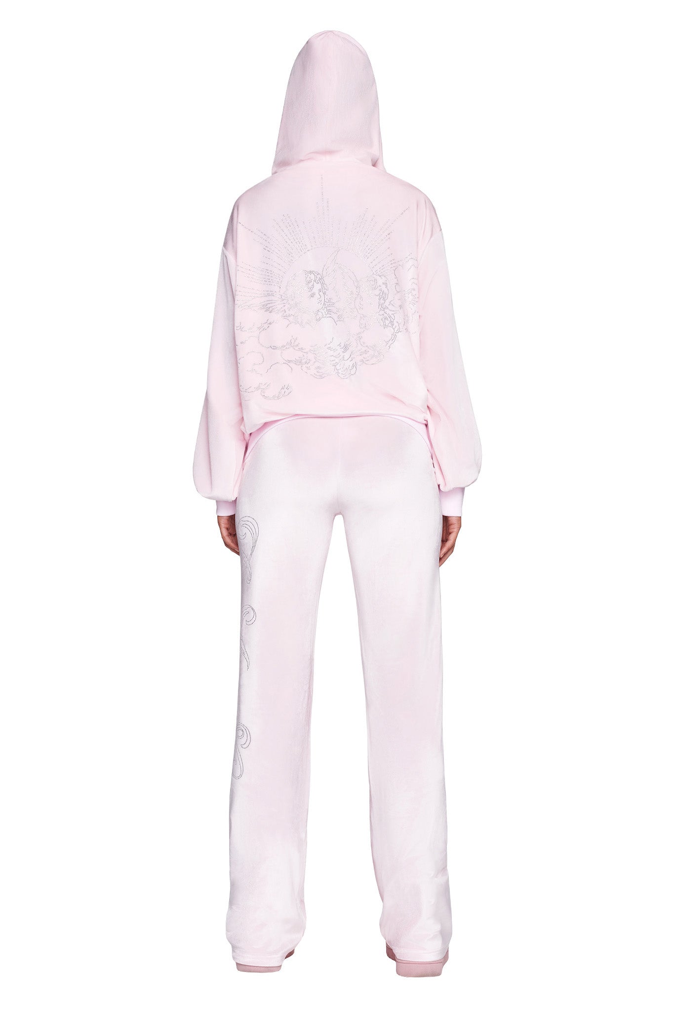 A person wearing a pink I.AM.GIA hooded jacket and the DARIA PANT - ICY PINK is shown from the back. The outfit features intricate designs, including celestial motifs, on both pieces. The hood is pulled up, obscuring the person's head.
