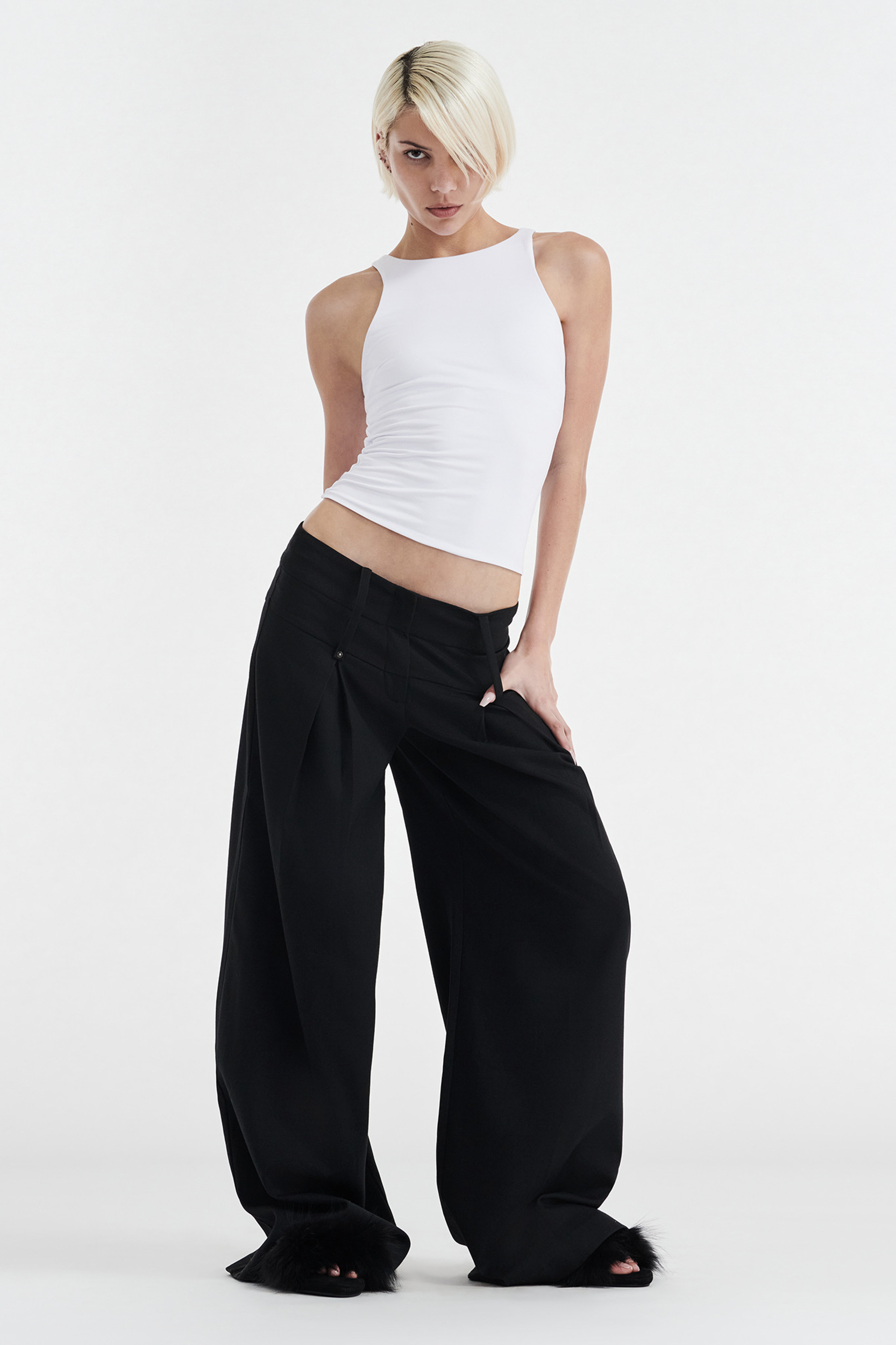 A person with short blonde hair models the CDP SOPHIE BASIC SLEEVELESS TANK WITH SHELF BRA in white and loose black pants, standing confidently against a plain white background.
