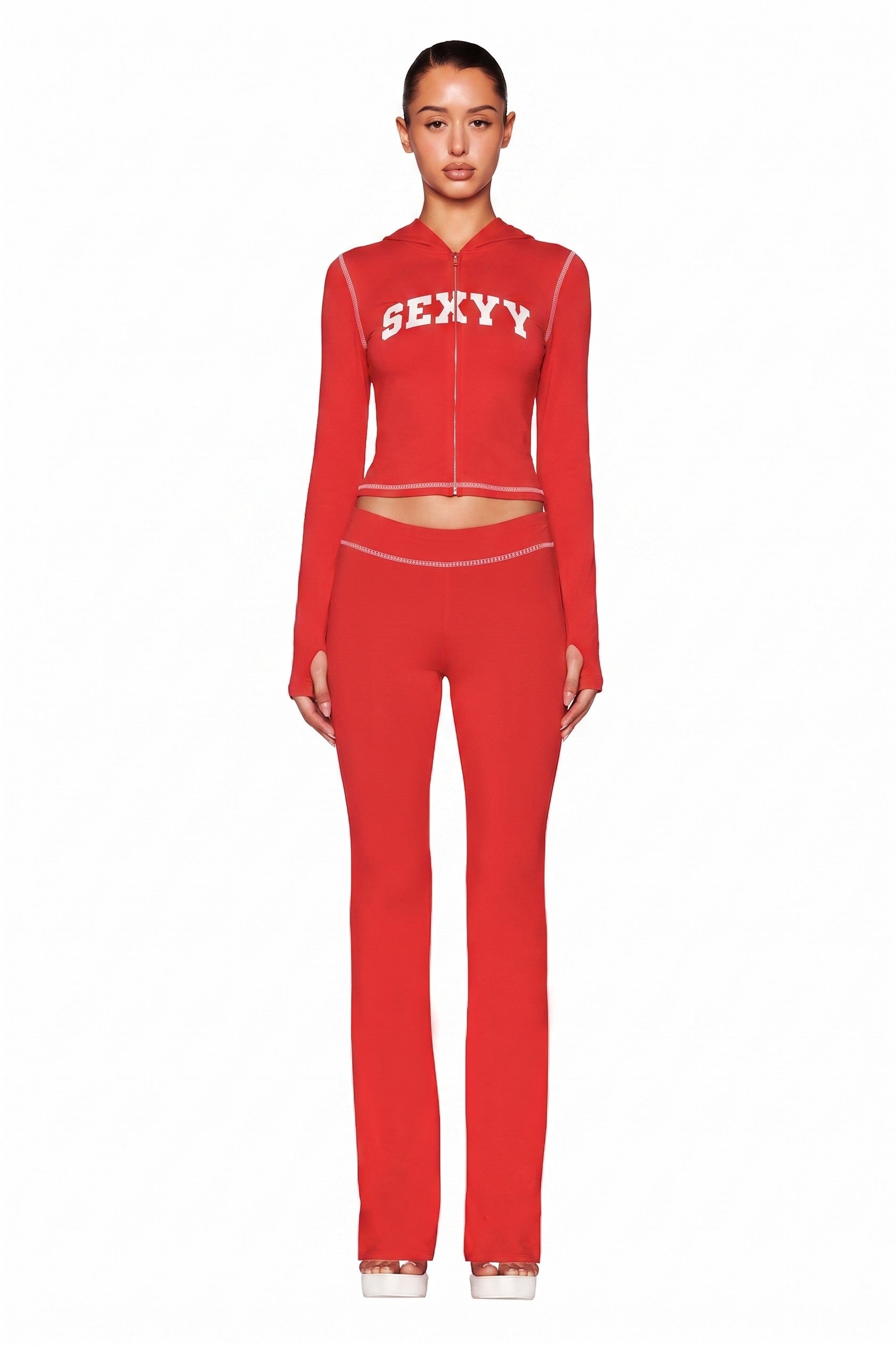 A woman faces forward in the I.AM.GIA X SEXYY RED BLARE TRACKPANT in red and a matching zip-up top with "SEXY" in white. She stands against a plain white background with her hair pulled back.