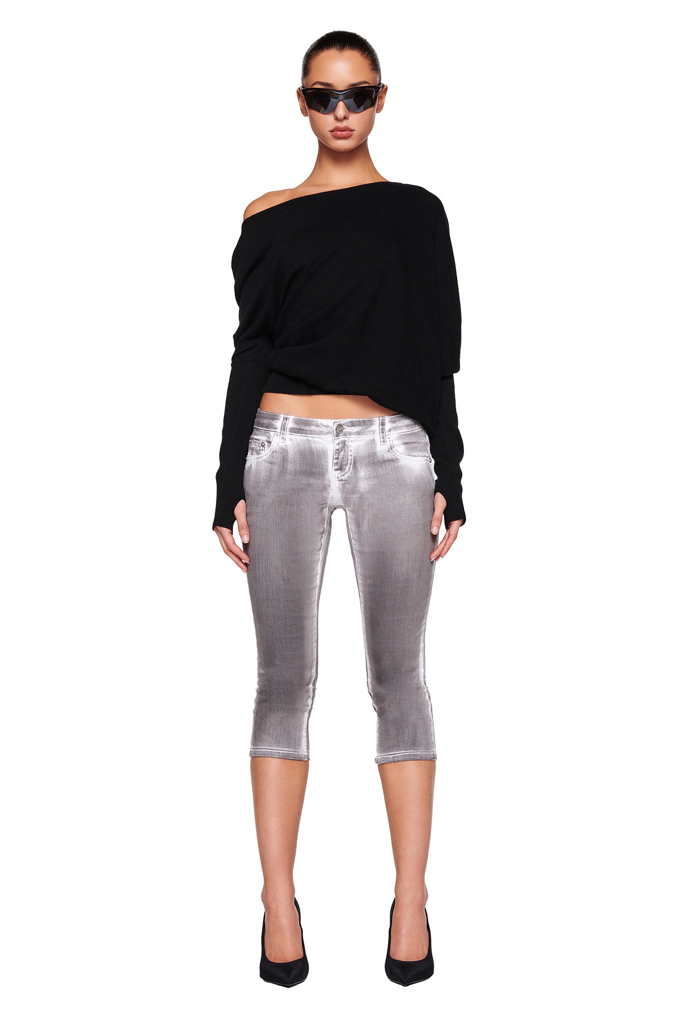 A person wears the GISELLE TOP in black from I.AM.GIA, light grey cropped jeans, black high heels, and dark sunglasses. They are standing against a white background, facing forward with a neutral expression.