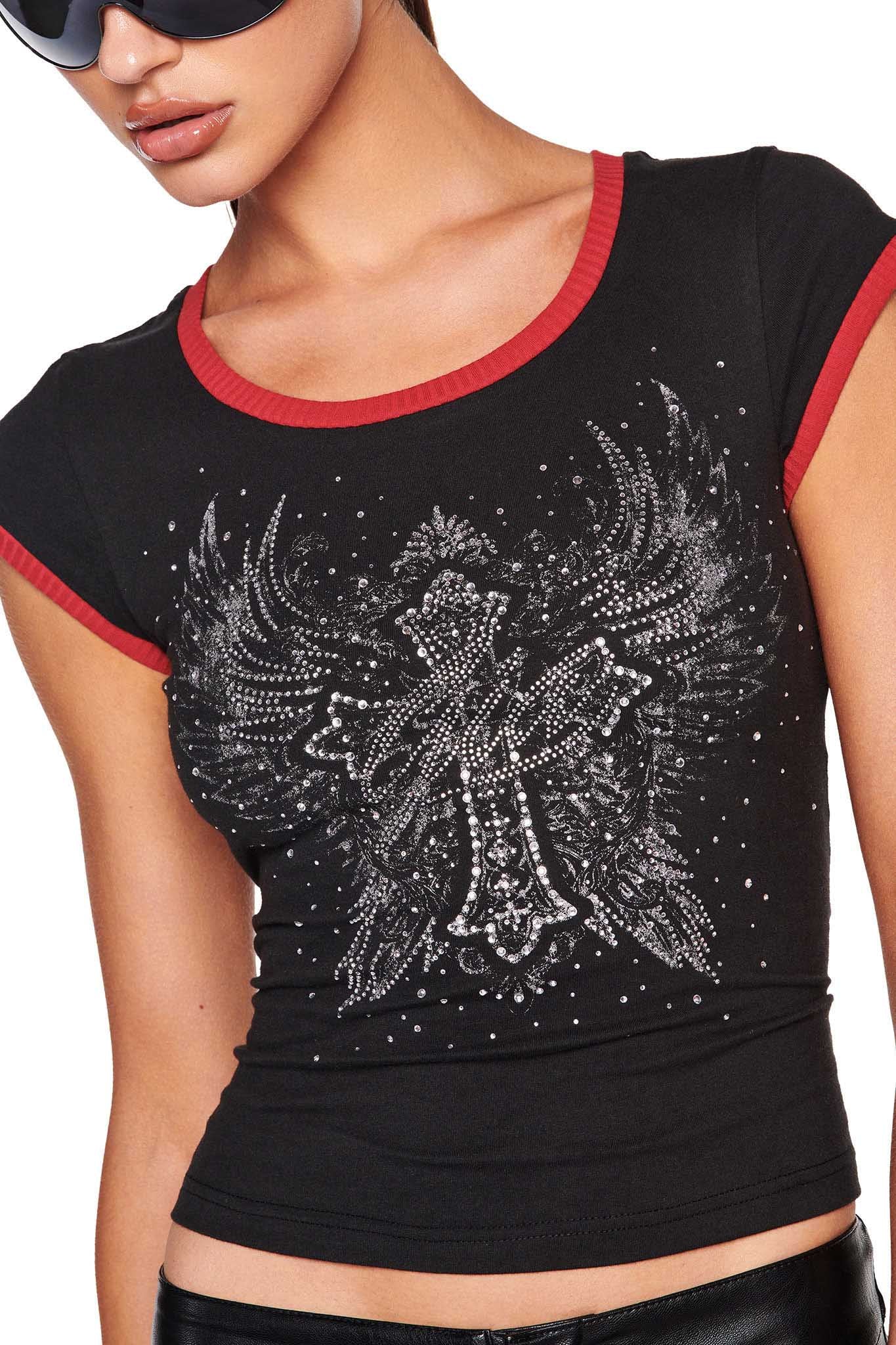 A person wearing the DORA TOP - BLACK from I.AM.GIA, featuring a sleek, fitted design with red trim and an intricate silver centerpiece depicting an abstract bird with outstretched wings surrounded by small sparkling dots. They are also sporting large, dark sunglasses.