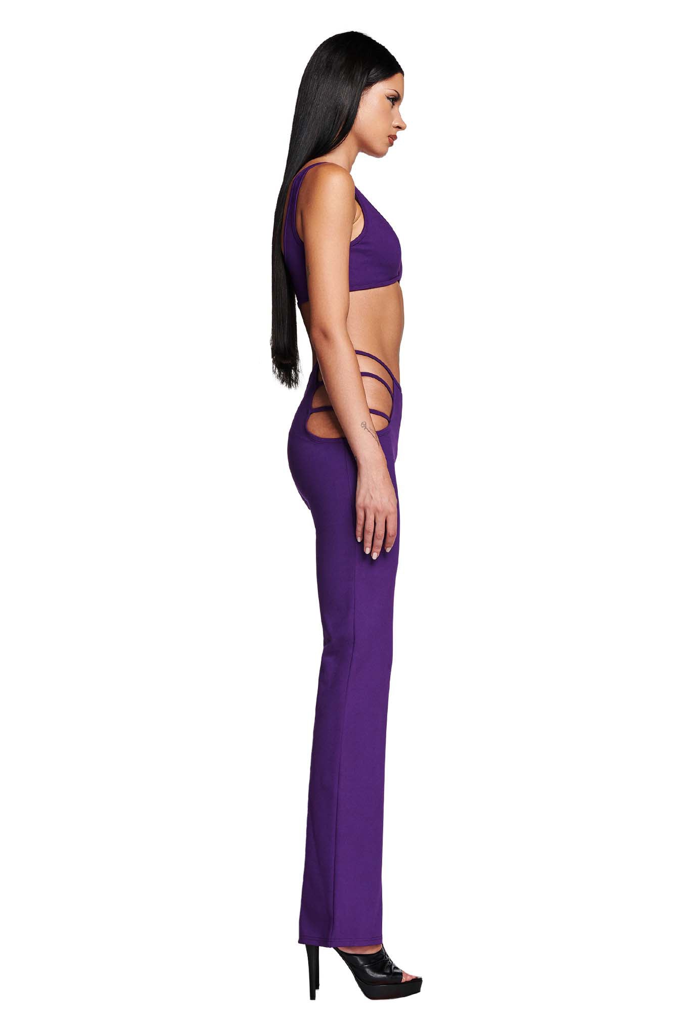 A woman with long, straight hair is posed in profile against a white background, wearing a fitted purple LUCID TOP from I.AM.GIA and matching pants featuring cut-out details at the hips. She completes the look with high-heeled open-toe shoes.