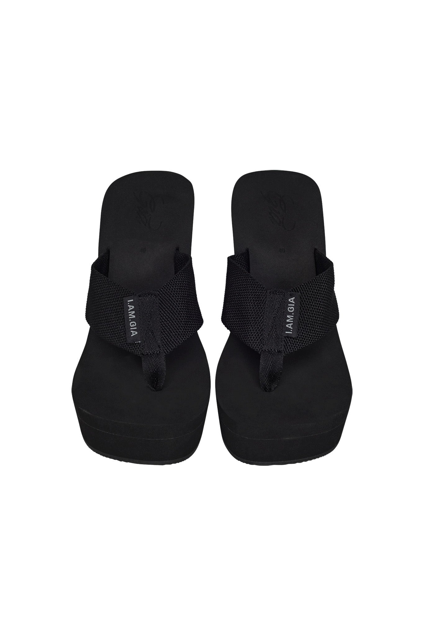 A pair of SHELBY FLIP FLOP - BLACK flip-flops featuring wide, fabric straps and emblazoned with the I.AM.GIA brand name. These black platform flip-flops boast thick soles and a simple yet stylish design, embodying I.AM.GIA's edgy aesthetic.