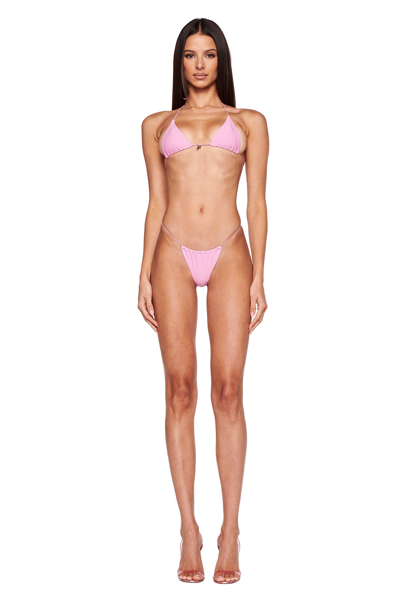 A woman with long, straight, dark hair is modeling the I.AM.GIA BAMBI Bikini Top in Bubblegum Pink on a white background. She stands straight with a relaxed posture and arms at her sides. The bikini consists of a triangular top and simple bottoms with thin straps. She wears clear high heels.