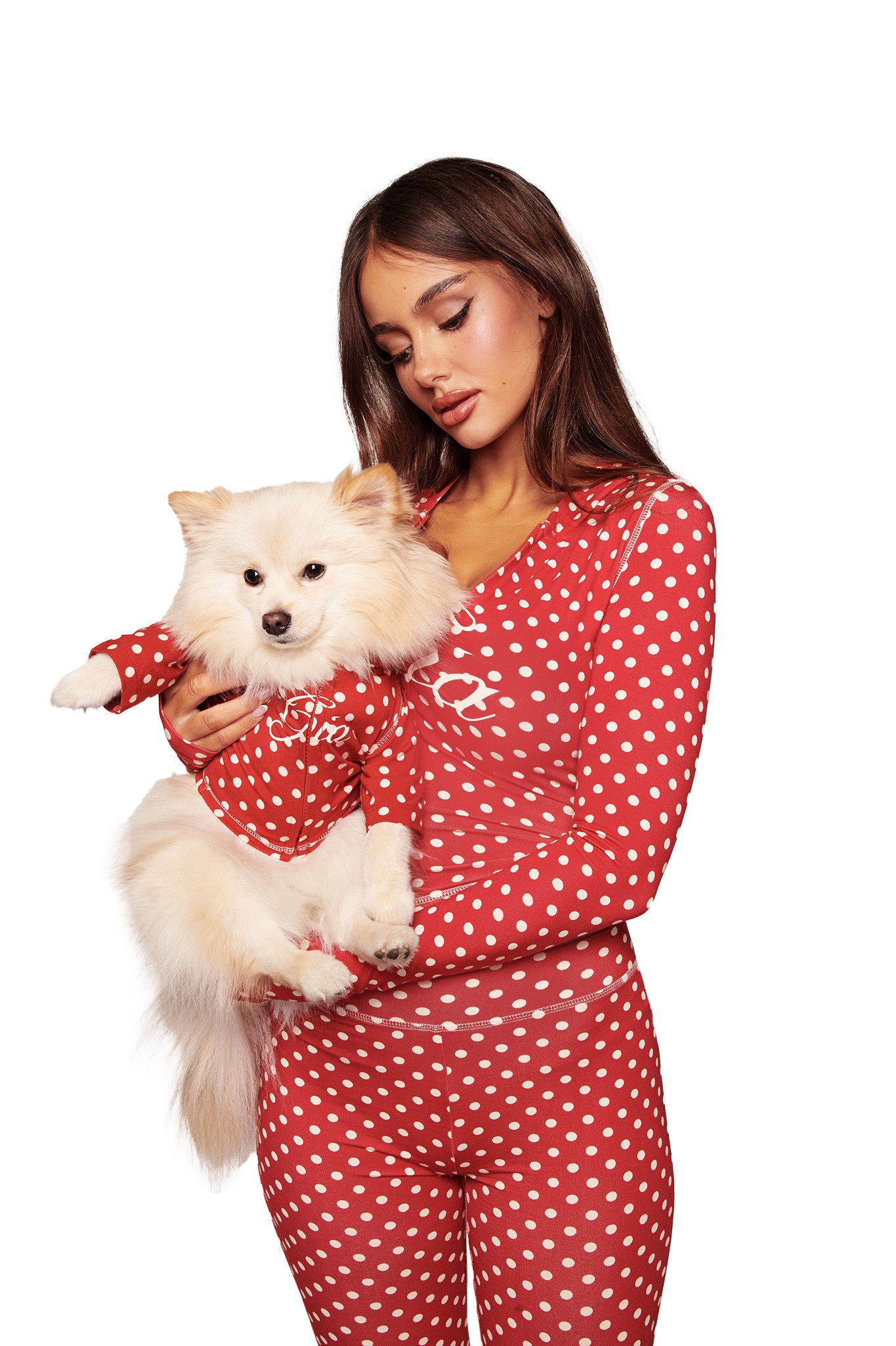 A woman wears red and white polka dot pajamas while holding a fluffy white dog in the I.AM.GIA BLARE BEST FRIEND DOG HOODIE - RED POLKA DOT, both facing forward against a plain white background.