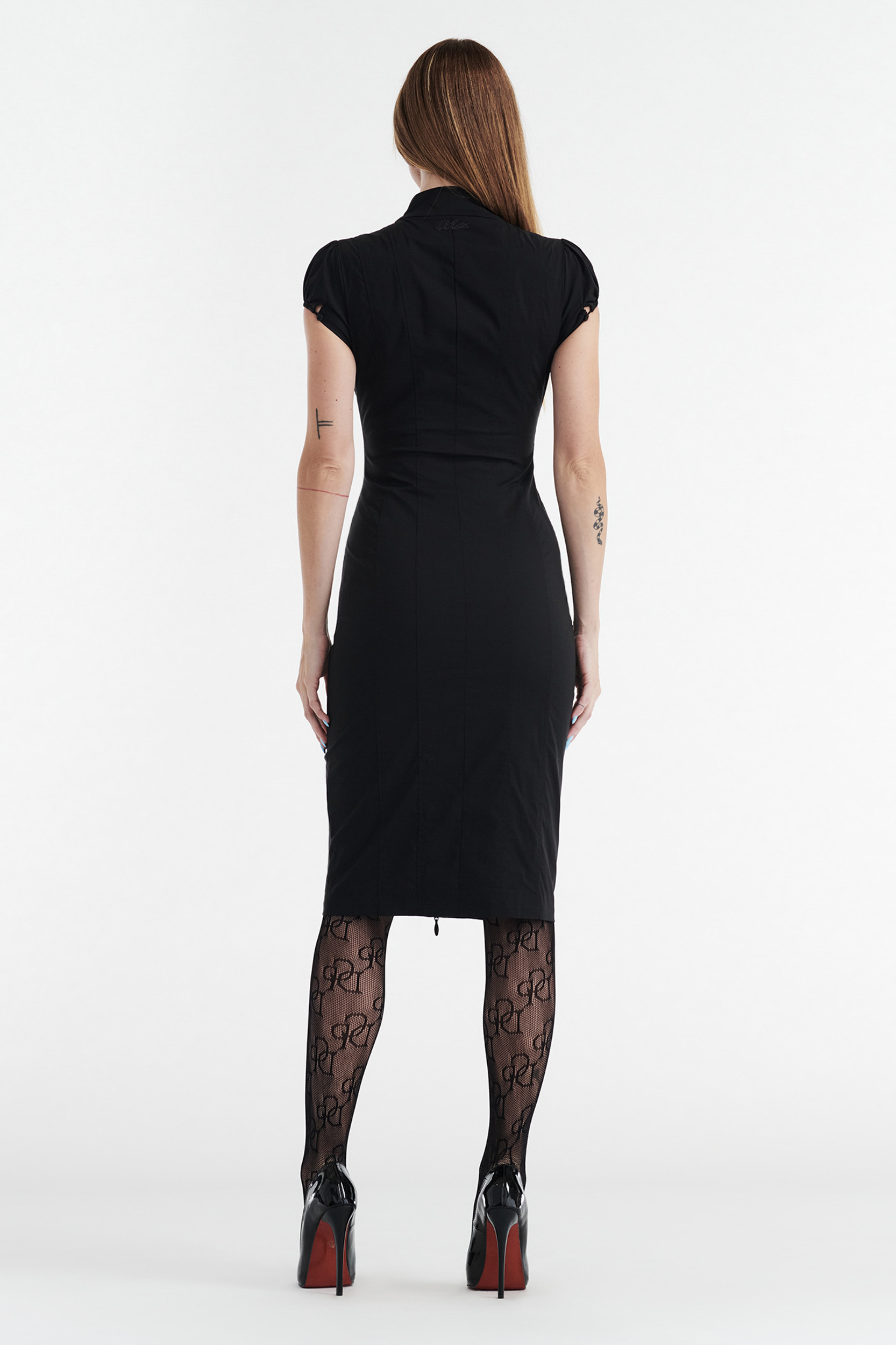 A woman with straight, long hair models the CDP COLETTE Panelled Puff Sleeve Midi Dress in black, paired with patterned tights and black heels. She stands facing away, arms relaxed, against a plain white background.