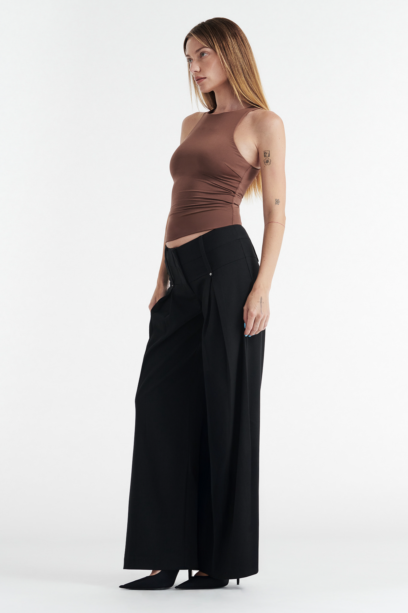 A woman stands sideways wearing the CDP SOPHIE BASIC SLEEVELESS TANK WITH SHELF BRA in chocolate, paired with high-waisted, wide-leg black pants and black pointed-toe shoes against a plain white background.