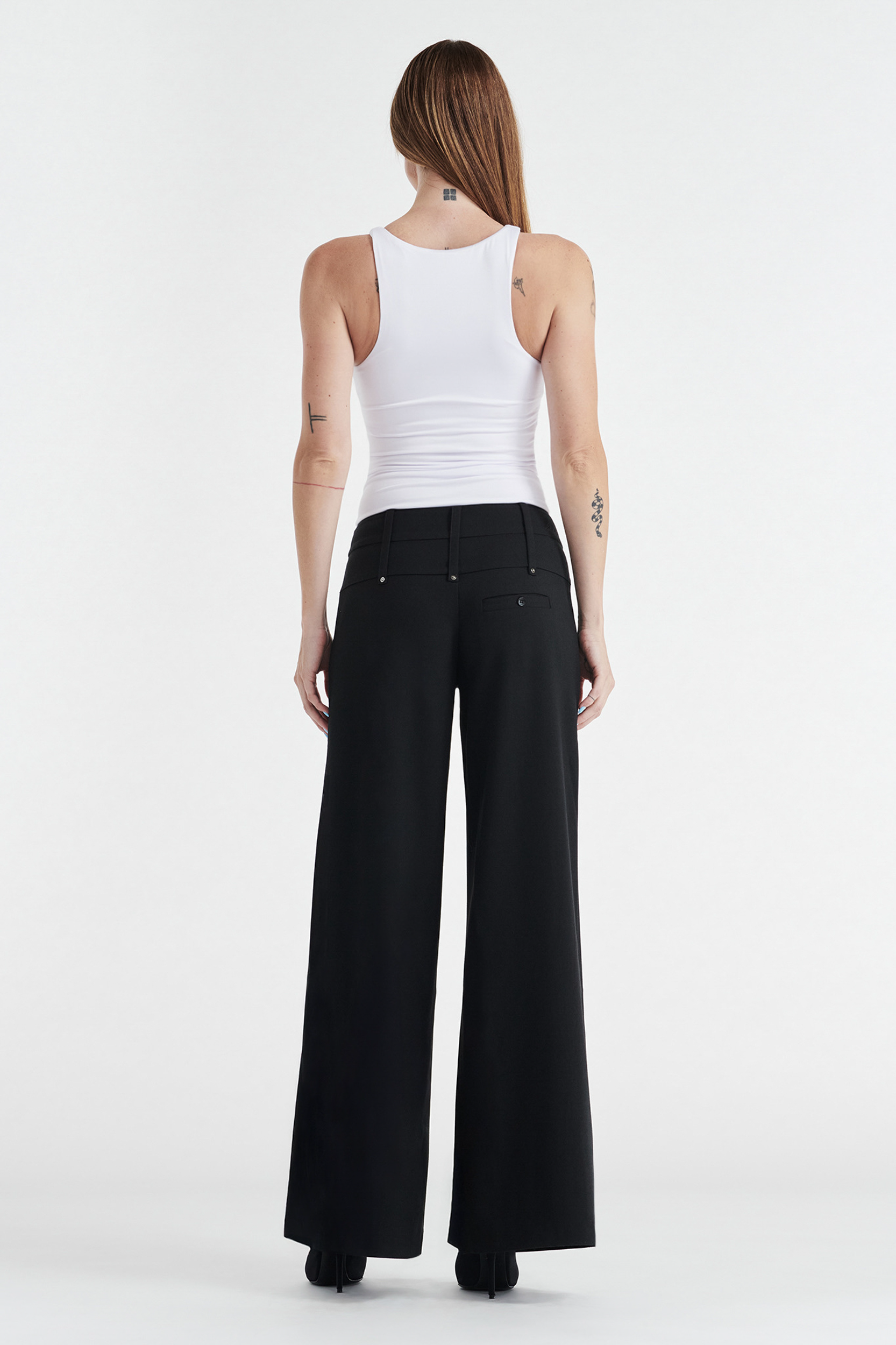 A person with long straight hair, wearing the CDP SOPHIE BASIC SLEEVELESS TANK WITH SHELF BRA in white and high-waisted black wide-leg pants, stands facing away from the camera against a plain white background.