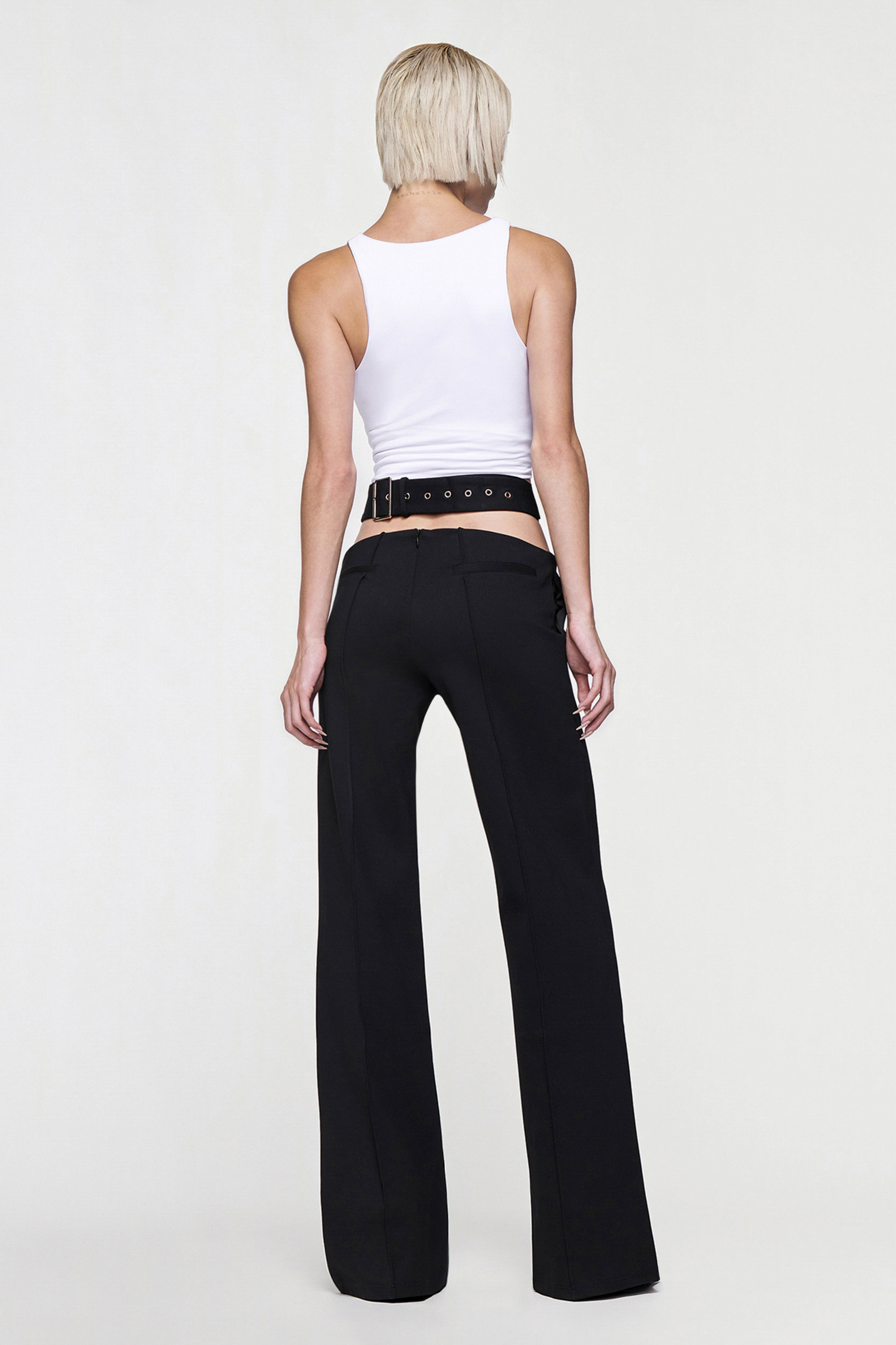 A person with short blonde hair, wearing a white sleeveless top and CDP's JULIETTE WIDE LEG PANT in black, stands facing away against a plain light background.