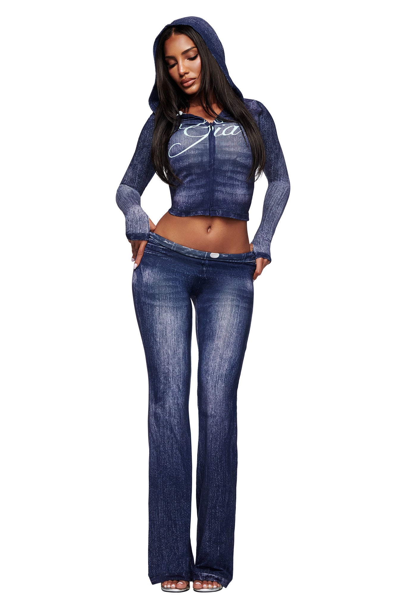A woman poses against a white background wearing I.AM.GIA’s BLARE TRACKPANT in dark denim with a matching blue, hooded, long-sleeve crop top, one hand on her hip.