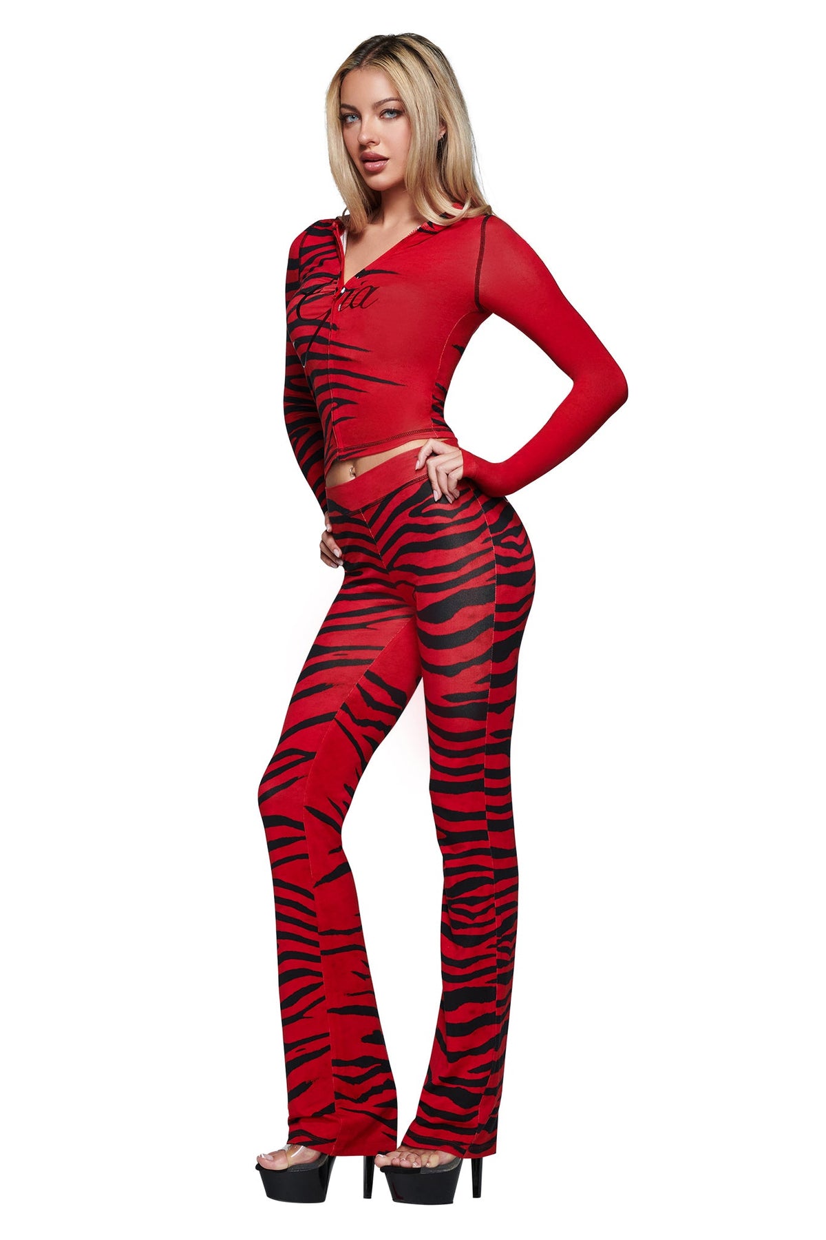 A woman poses with one hand on her hip, wearing the I.AM.GIA BLARE HOODIE in the signature Red Wild Side print with matching flared pants and black platform heels, set against a white background.