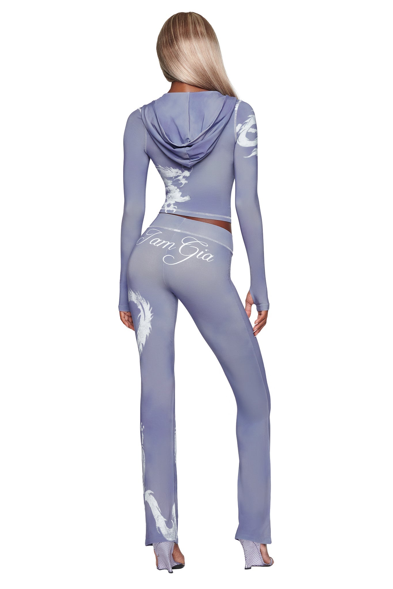 A person with long blonde hair wears the I.AM.GIA BLARE HOODIE in steel blue dragon, a fitted two-piece outfit featuring a hood and white dragon designs. The word “I.AM.GIA” appears on the back as the person stands with their back to the camera.
