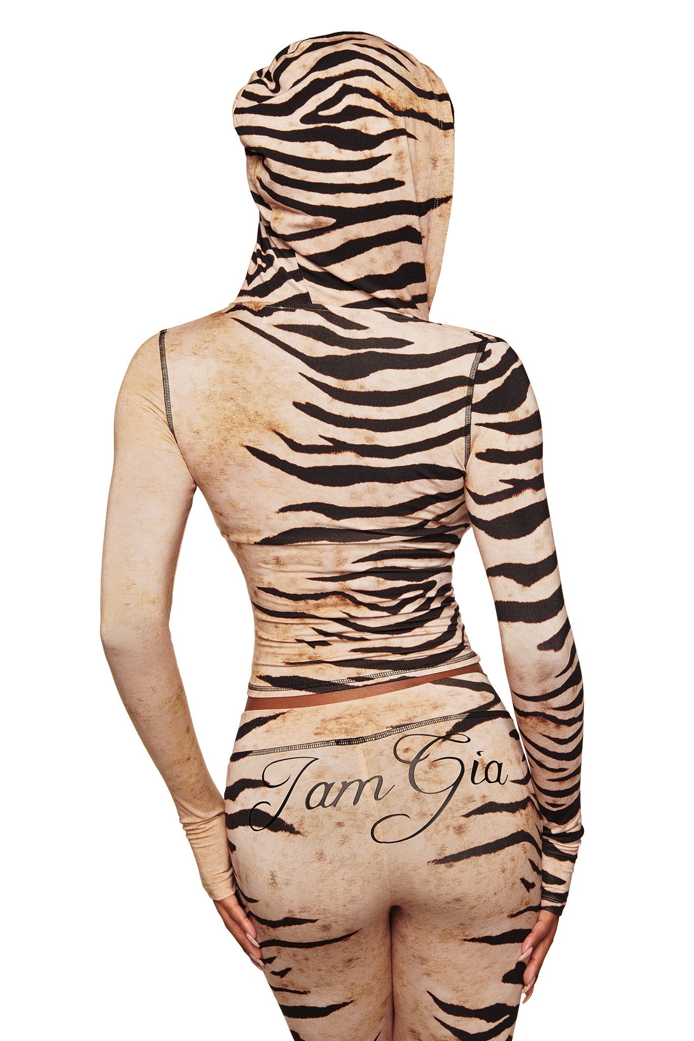 A person is seen from the back wearing I.AM.GIA’s BLARE TRACKPANT in Wild Side, a tiger-striped, form-fitting hooded outfit with "I.AM.GIA" scripted on the lower back.