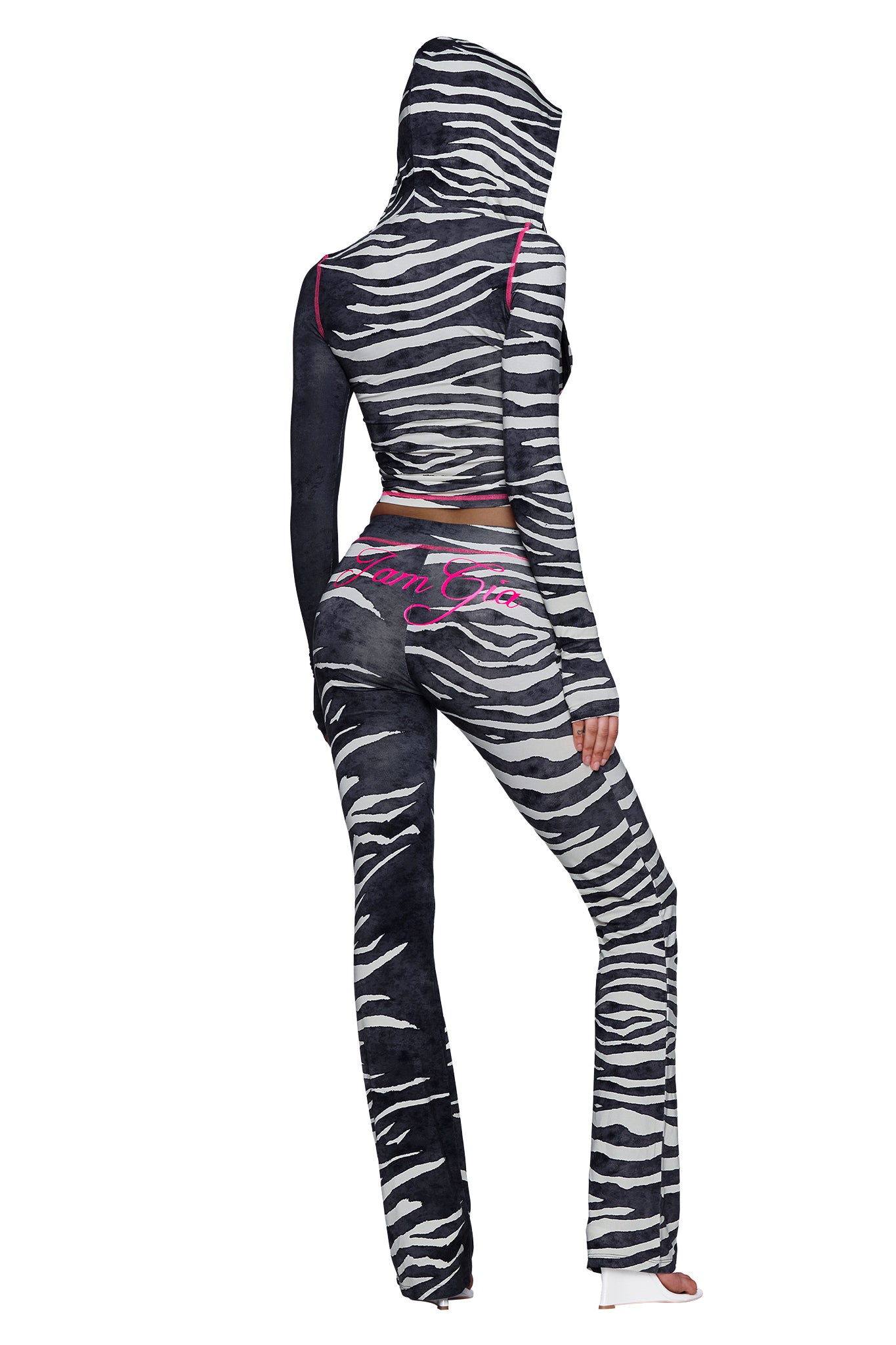 A person wearing the I.AM.GIA BLARE TRACKPANT - BLACK WILD SIDE with a zebra print hoodie featuring pink text, standing with their back facing the camera. The outfit has a fitted style and is paired with white shoes.