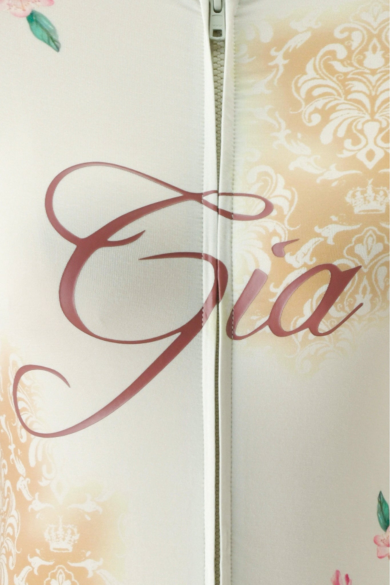 Close-up of the BLARE HOODIE - BLOSSOM by I.AM.GIA, featuring a blossom print with a white zipper, beige floral patterns, pink flowers, and “I.AM.GIA” written in large, cursive pink letters across the front.