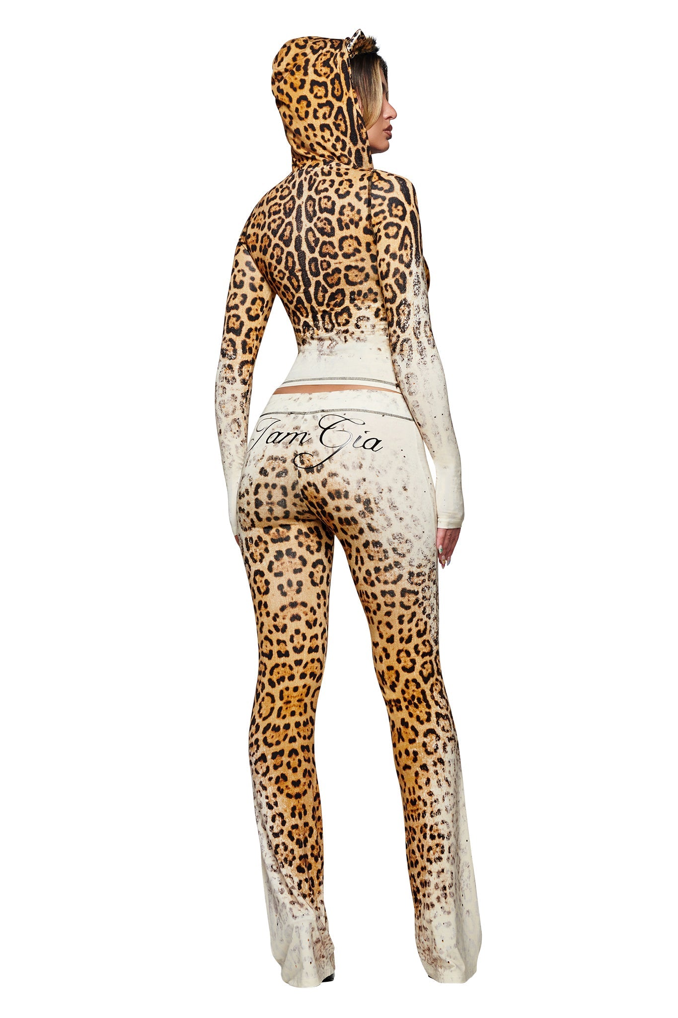 A person stands facing away, dressed in a hooded, full-body outfit with a bold cream faded panther print similar to the I.AM.GIA BLARE TRACKPANT. “Vam Gia” is written on the back of the suit, which features a flared pant silhouette and a hood that completely covers their hair. The plain white background keeps the focus on the striking design.
