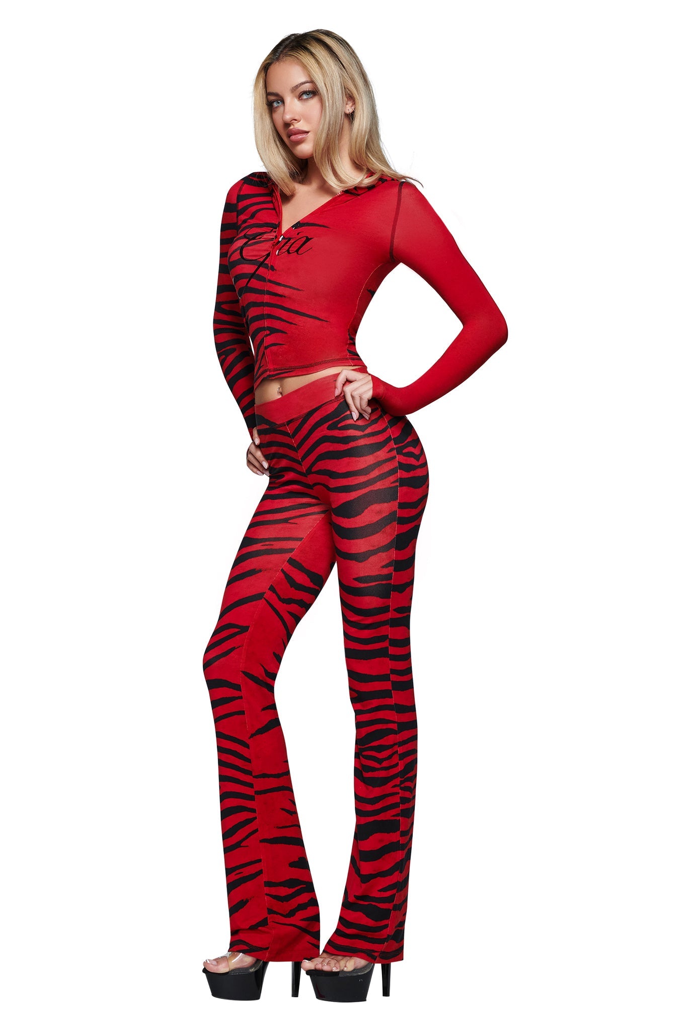 Model wears the I.AM.GIA BLARE HOODIE - RED WILD SIDE, featuring red and black tiger stripes, long sleeves, and a soft bamboo fabrication. She pairs the look with flared pants and black platform heels against a white background.
