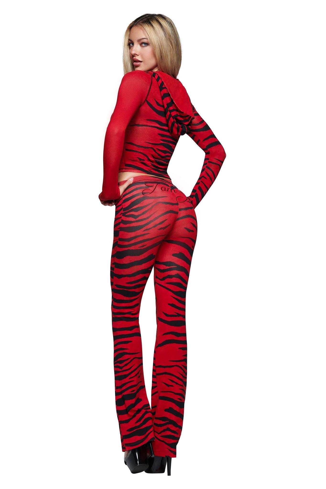 A person stands posing in the I.AM.GIA BLARE HOODIE in the vibrant Red Wild Side print, featuring long sleeves. They look over their shoulder, wearing matching flared pants, black high heels, and have long blonde hair.
