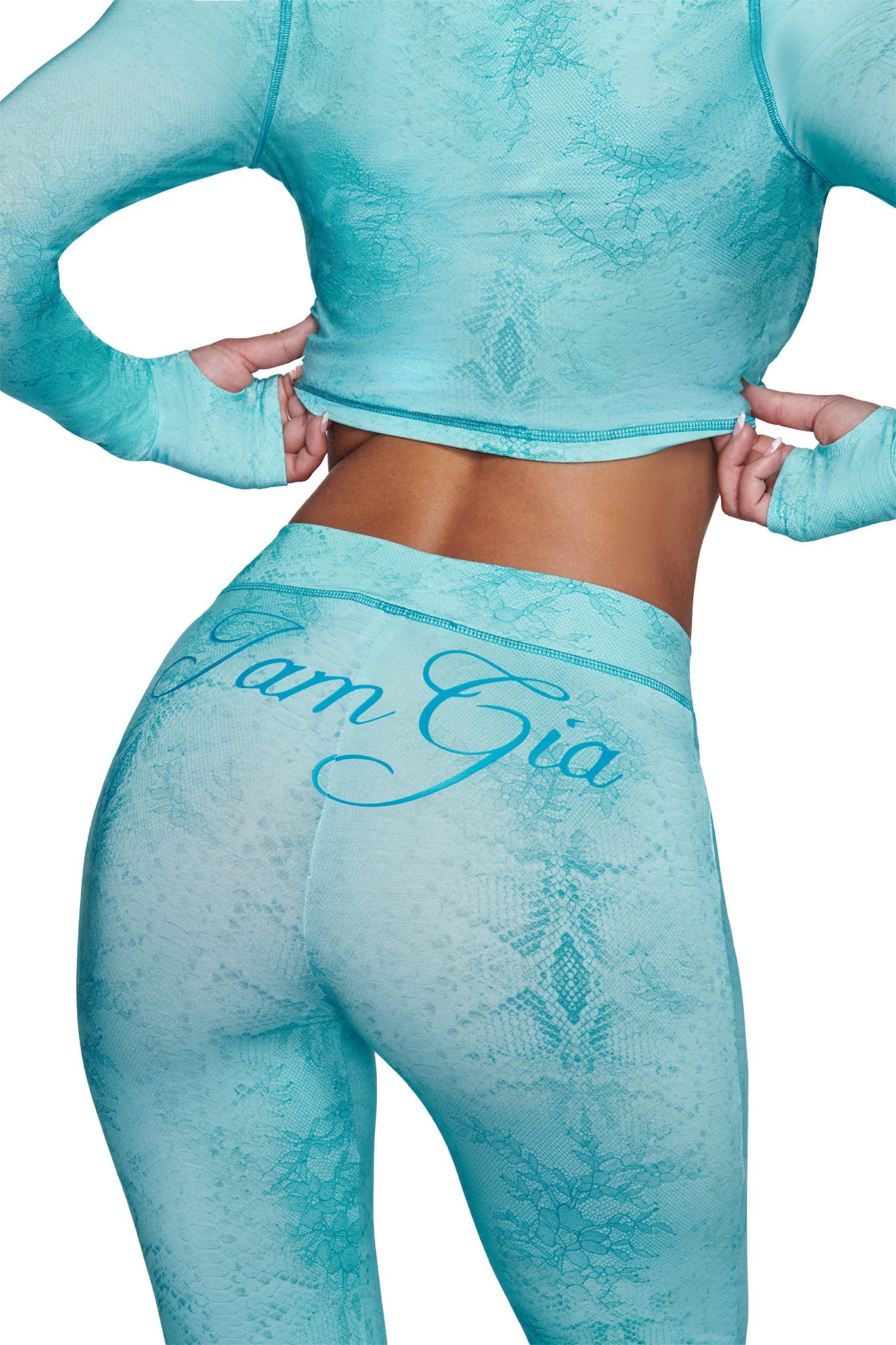 A person models the I.AM.GIA BLARE TRACKPANT - TEAL SERPENTINE and a matching fitted, long-sleeve crop top; “I.AM.GIA” is visible on the waistband. The image shows their back from shoulders to knees.