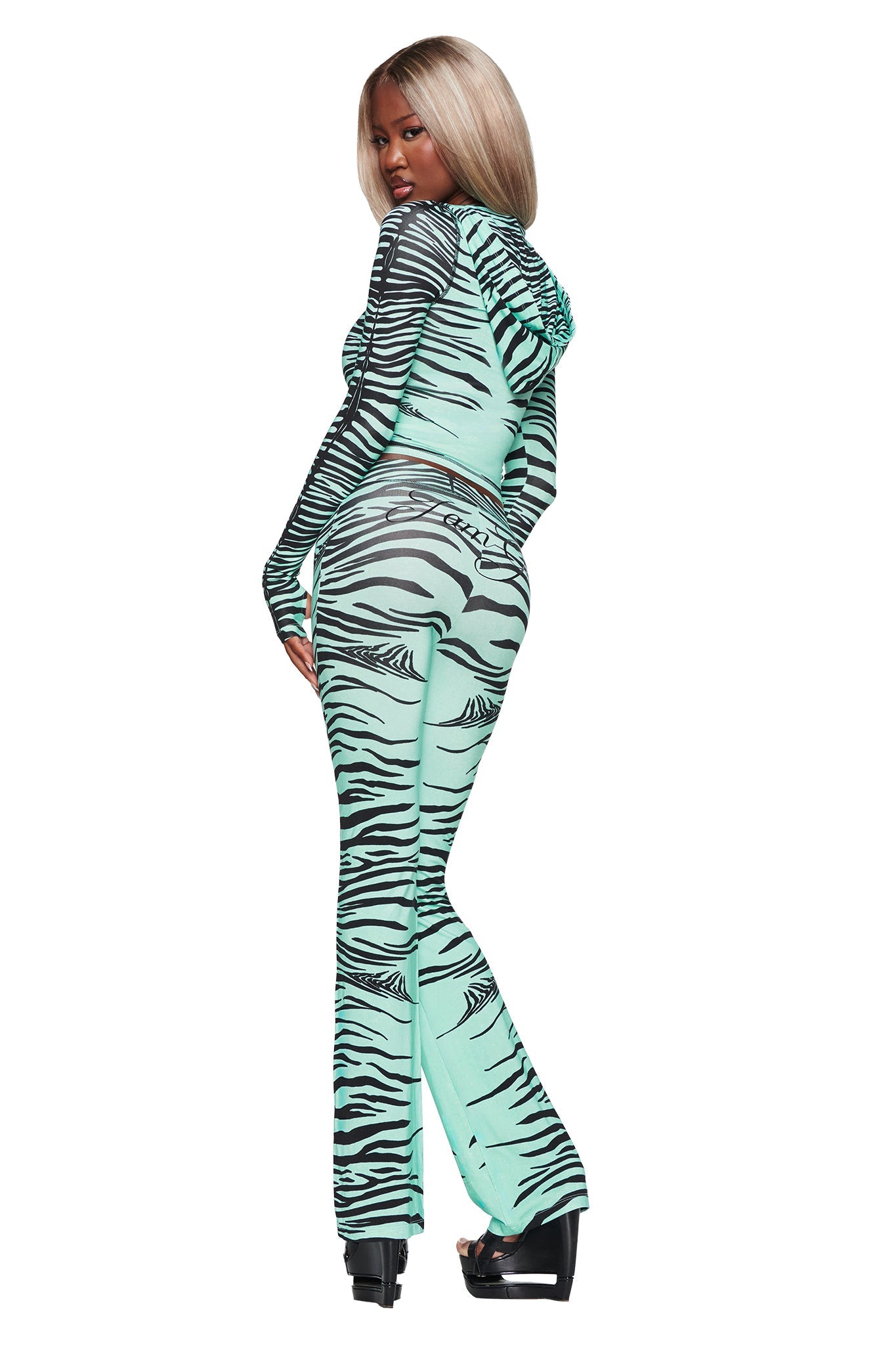 A person with long blonde hair wears the I.AM.GIA BLARE HOODIE in Aqua Fine Line Zebra, paired with matching pants and platform heels, standing with their back turned and looking over their shoulder.