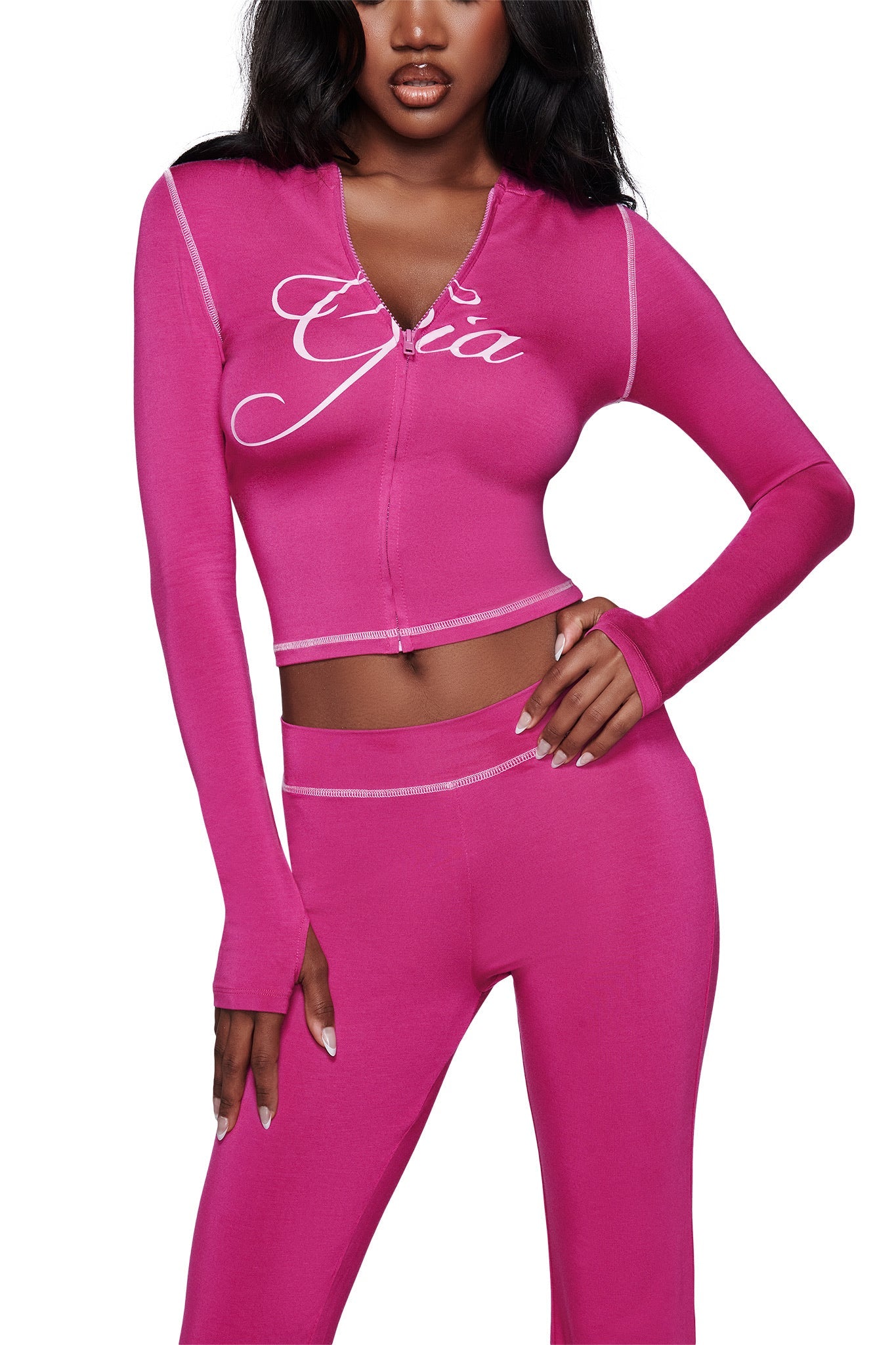 A woman wears the I.AM.GIA BLARE HOODIE in raspberry with matching pants. The fitted, long-sleeve top features white stitching and "Gia" in cursive on the chest. Her loose dark hair completes the bold look.