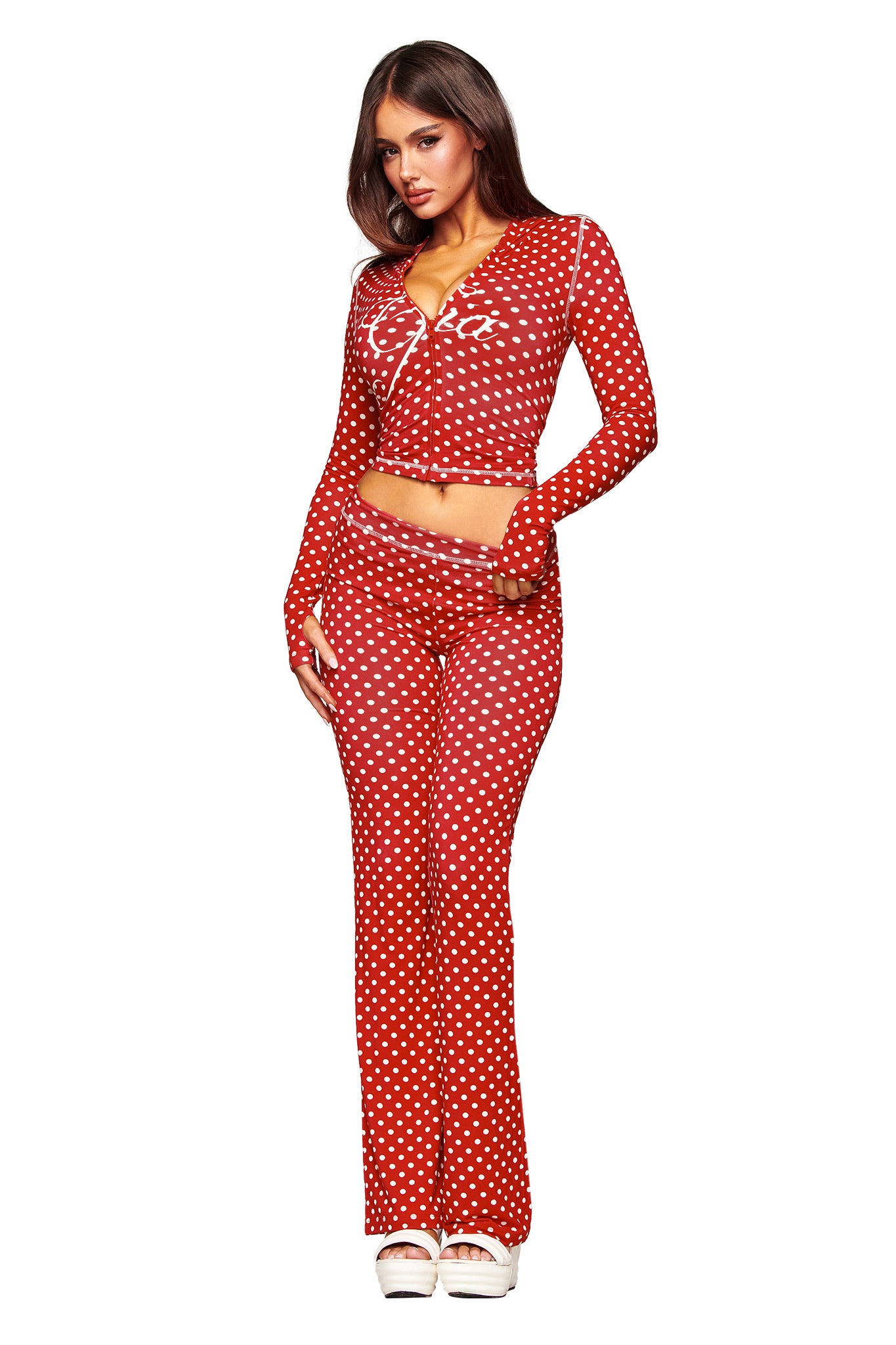 A woman stands against a white background wearing I.AM.GIA's BLARE TRACKPANT in red polka dot with a matching long-sleeve, button-up crop top and white platform shoes.