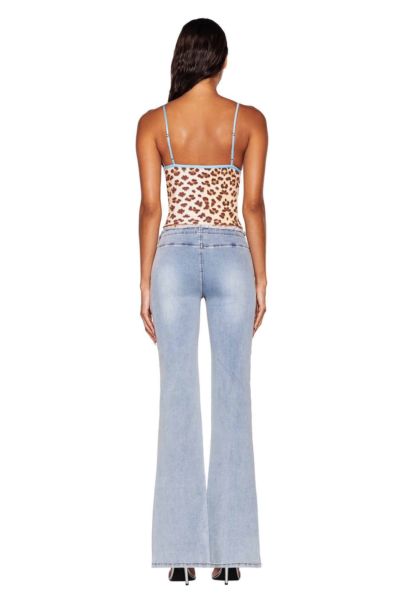 A woman with long dark hair is wearing the EDITA TOP by I.AM.GIA in a neutral leopard pattern, complete with adjustable straps, along with light blue flared jeans. She is facing away from the camera, and her outfit fits her like a second skin against a plain white background.