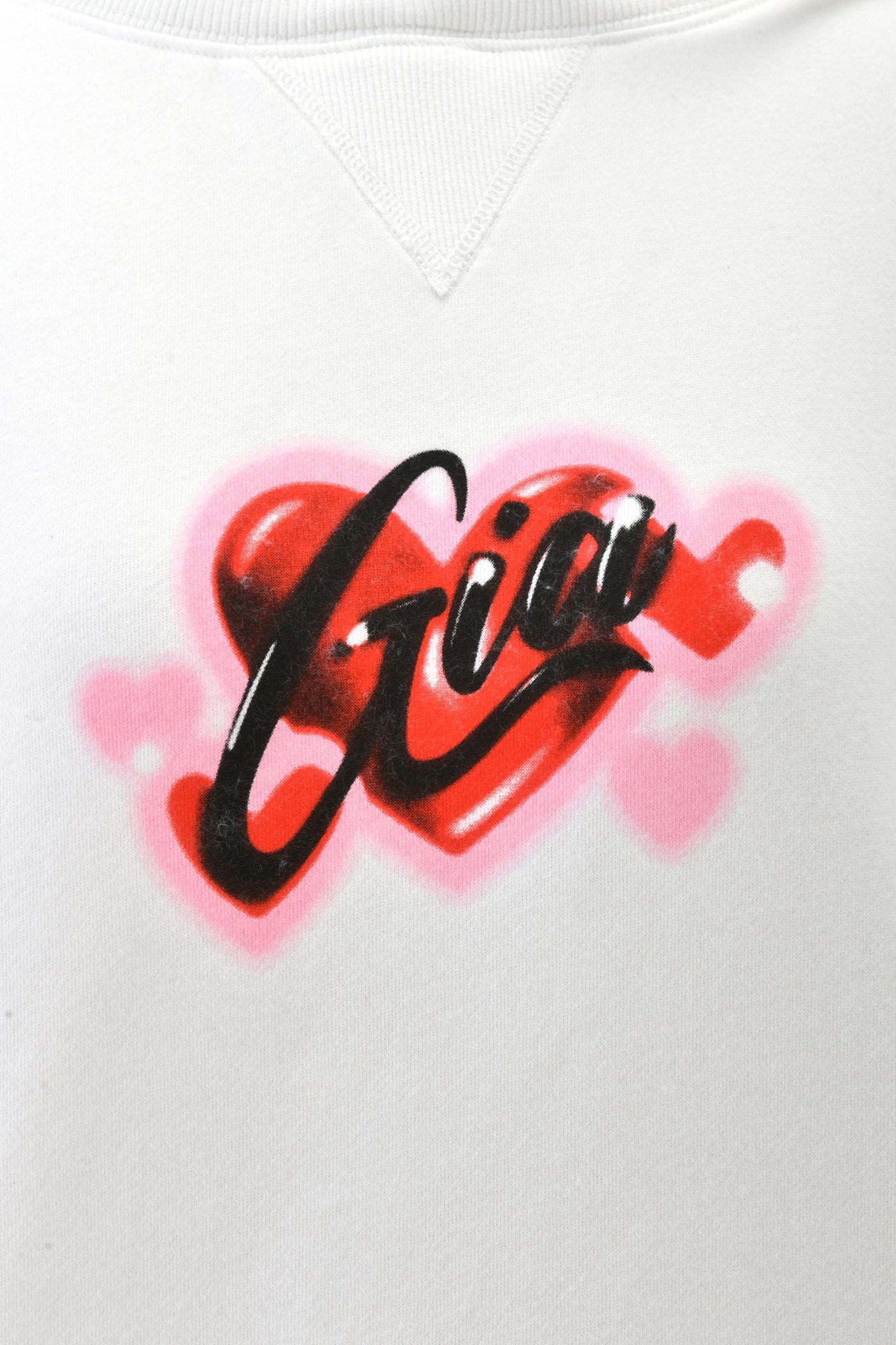 The DORIAN HOODIE - WHITE by I.AM.GIA is an oversized white hoodie featuring a bold "Gia" script, red heart, and pink accents inspired by airbrush art—an eye-catching statement piece.