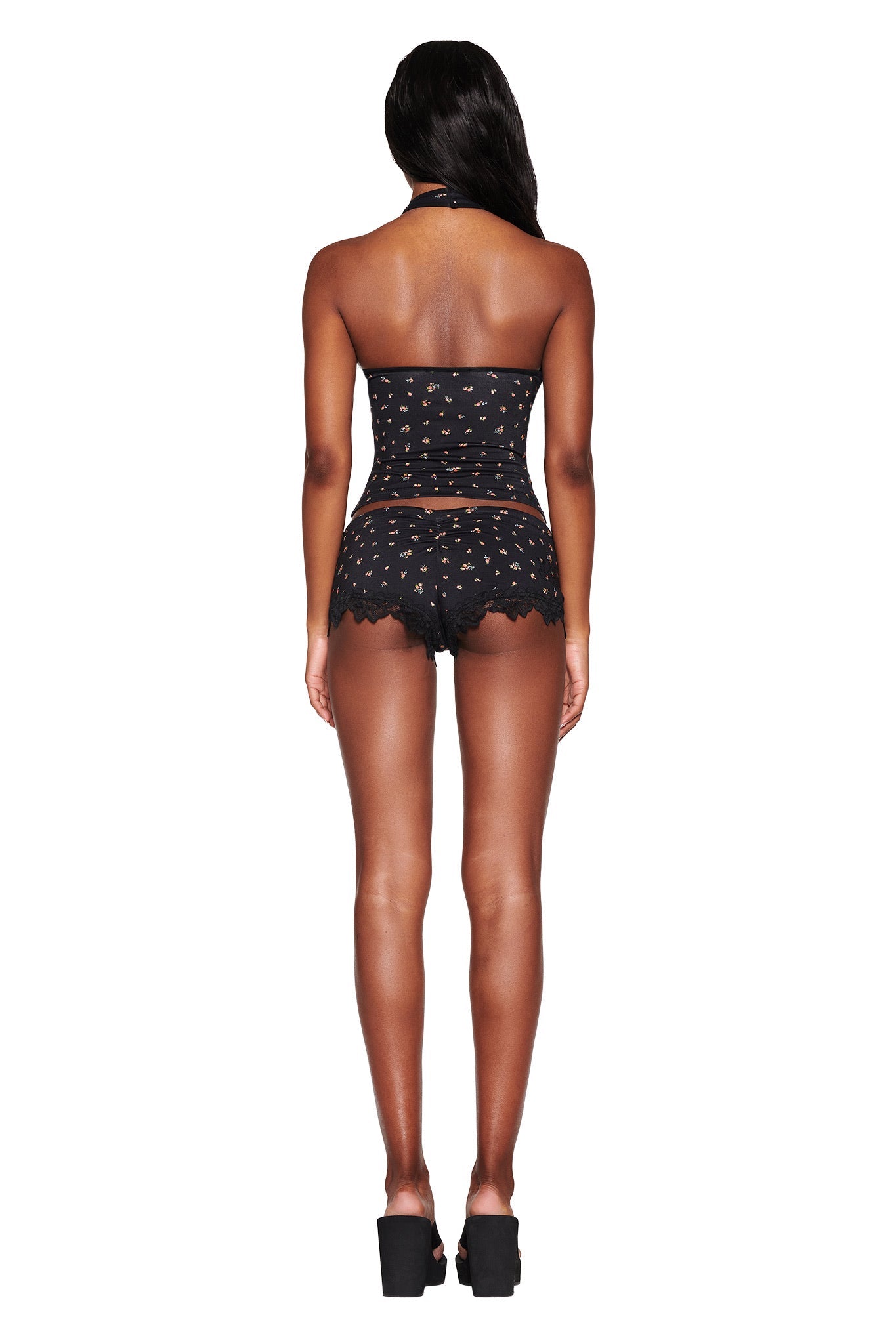 A person is seen from the back wearing an I.AM.GIA CELESTE TOP in DITSY FLORAL, paired with matching lace-detail shorts. The strapless, bodycon ensemble includes small cutouts and is complemented by platform heels against a white background.