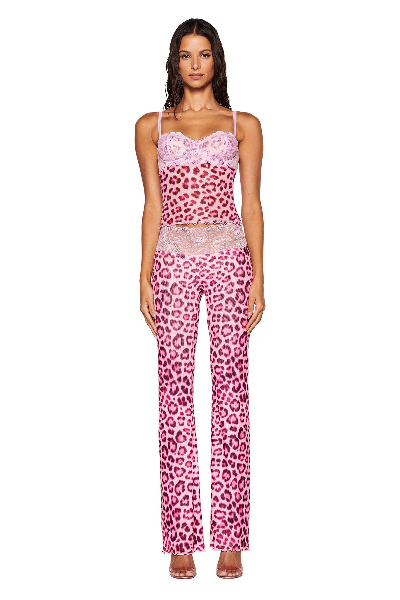 A woman stands wearing the I.AM.GIA SILO TOP in pink leopard print, featuring mesh fabrication. The ensemble includes a sheer camisole top and matching flared pants. She has long brown hair, minimal accessories, and is posing against a plain white background.