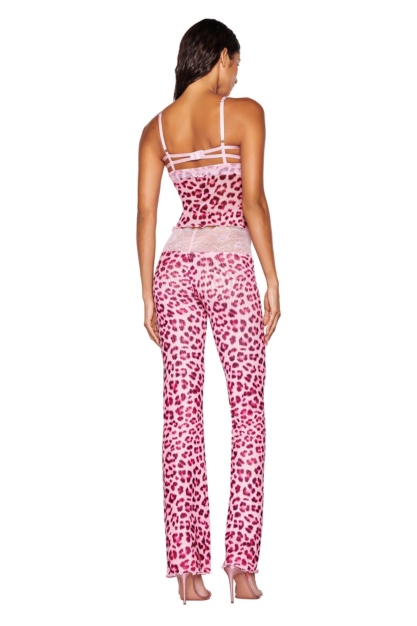 A person stands with their back to the camera, flaunting the SILO TOP in pink leopard print by I.AM.GIA. The outfit, crafted from mesh fabrication, is a bodycon fit featuring a fitted top and matching pants, perfectly paired with high heels. Their long hair cascades gracefully against the plain white backdrop.